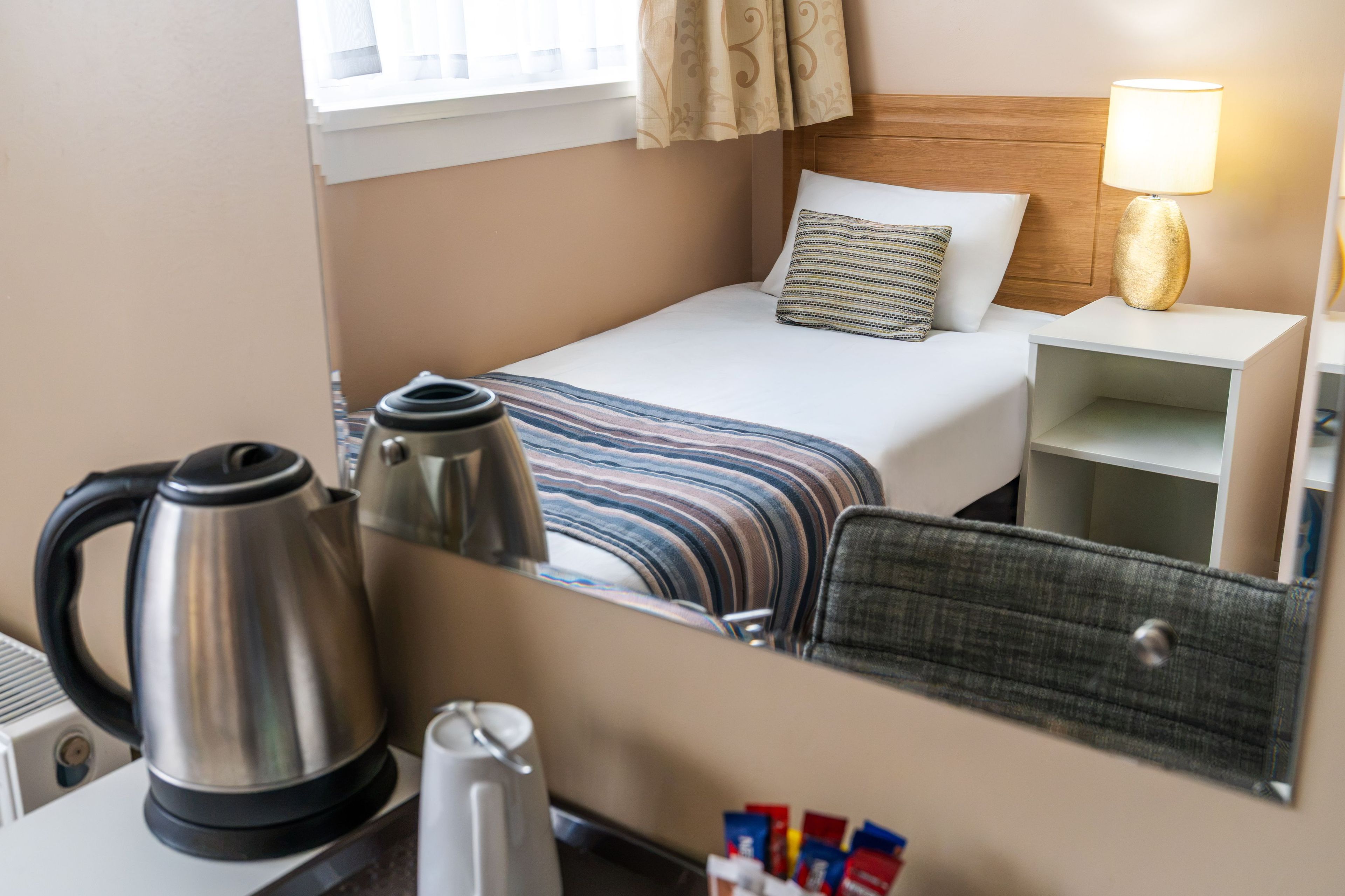 Een hotelkamer met een bed, een nachtkastje met een lamp, een koffiezetapparaat en een stoel.