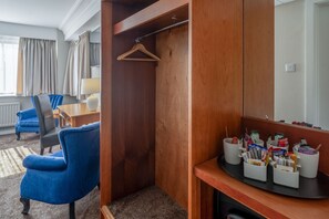 A hotel room with a wooden wardrobe, a desk with a chair, a hanging coat rack, and a coffee station with mugs and cups. - Grand Hotel Gosforth Park (Newcastle-upon-Tyne)