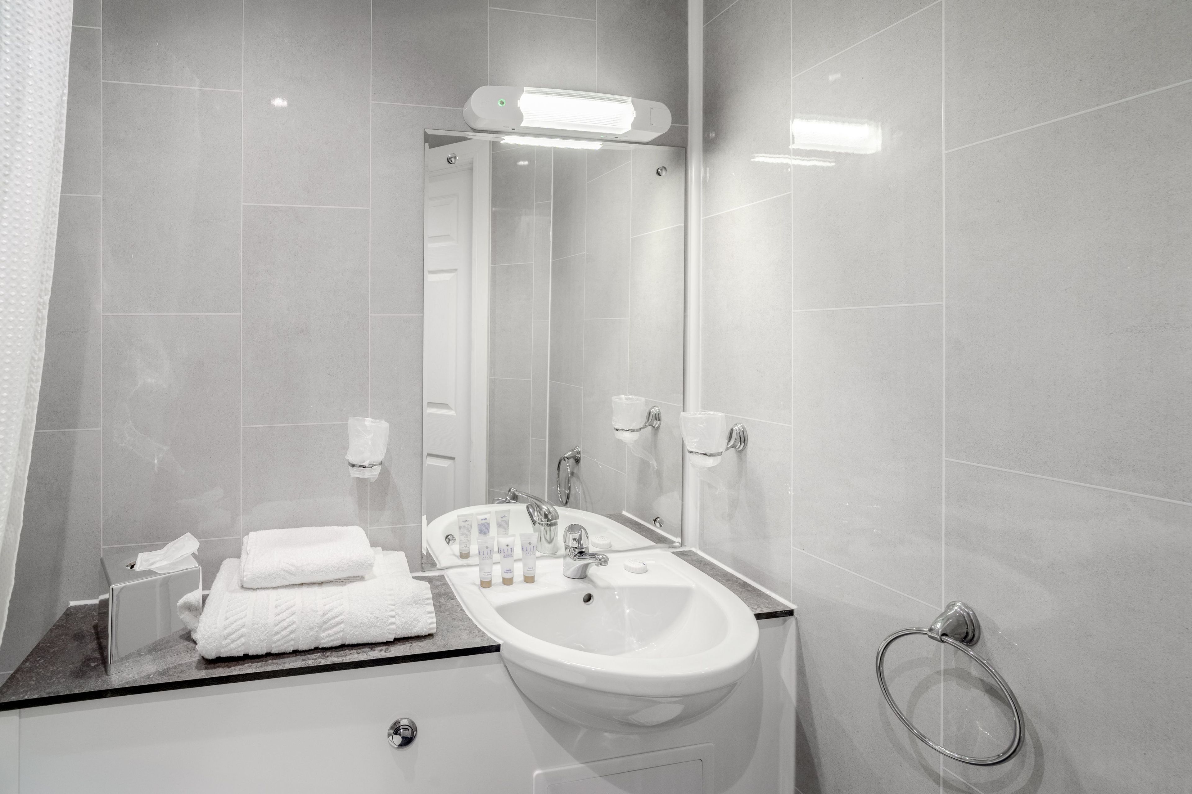 A modern bathroom with a white sink, mirror, and towel rack.