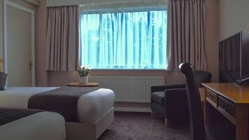 A hotel room with a bed, a desk with a computer, a chair, and a window with curtains.