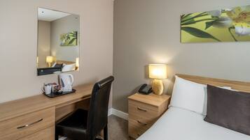 Et hotelværelse med seng, skrivebord med stol, telefon, lampe og kaffemaskine.