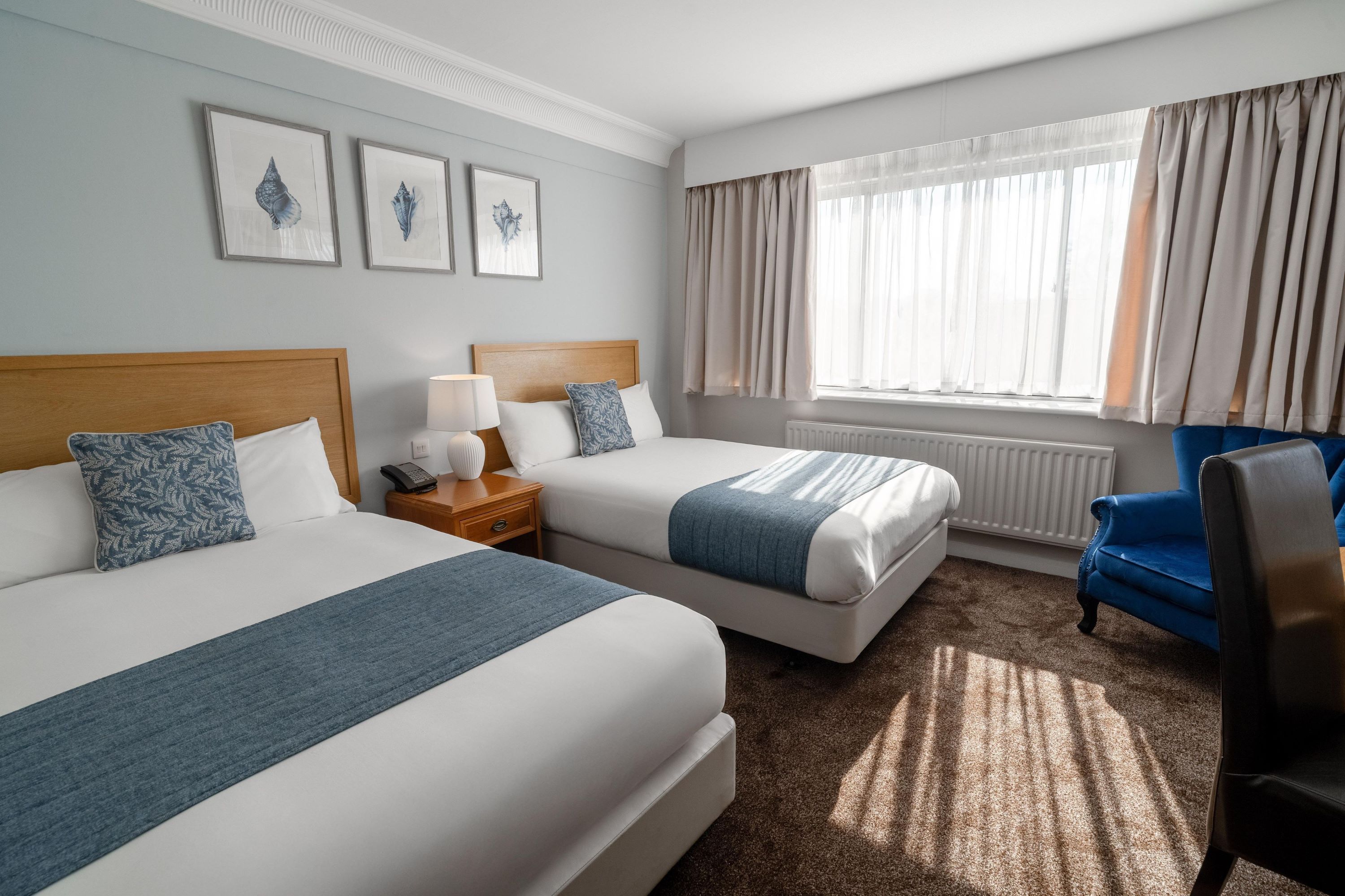A hotel room with two beds, a desk, a chair, and a window with curtains.