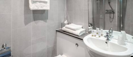 A modern bathroom with a glass shower enclosure, a white sink with toiletries, and a toilet.