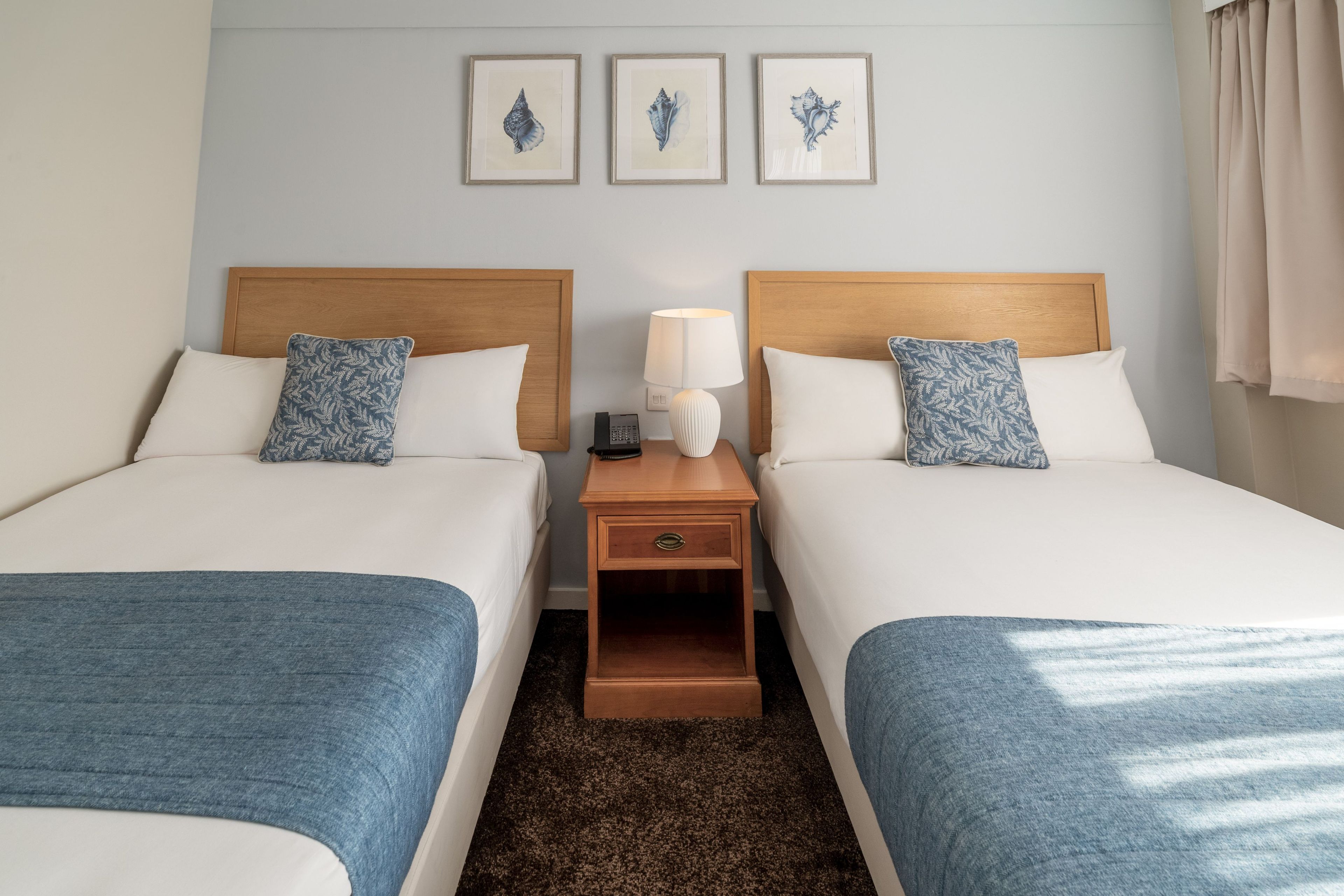 Une chambre d’hôtel avec deux lits, une table de chevet avec une lampe et trois tableaux encadrés au mur.