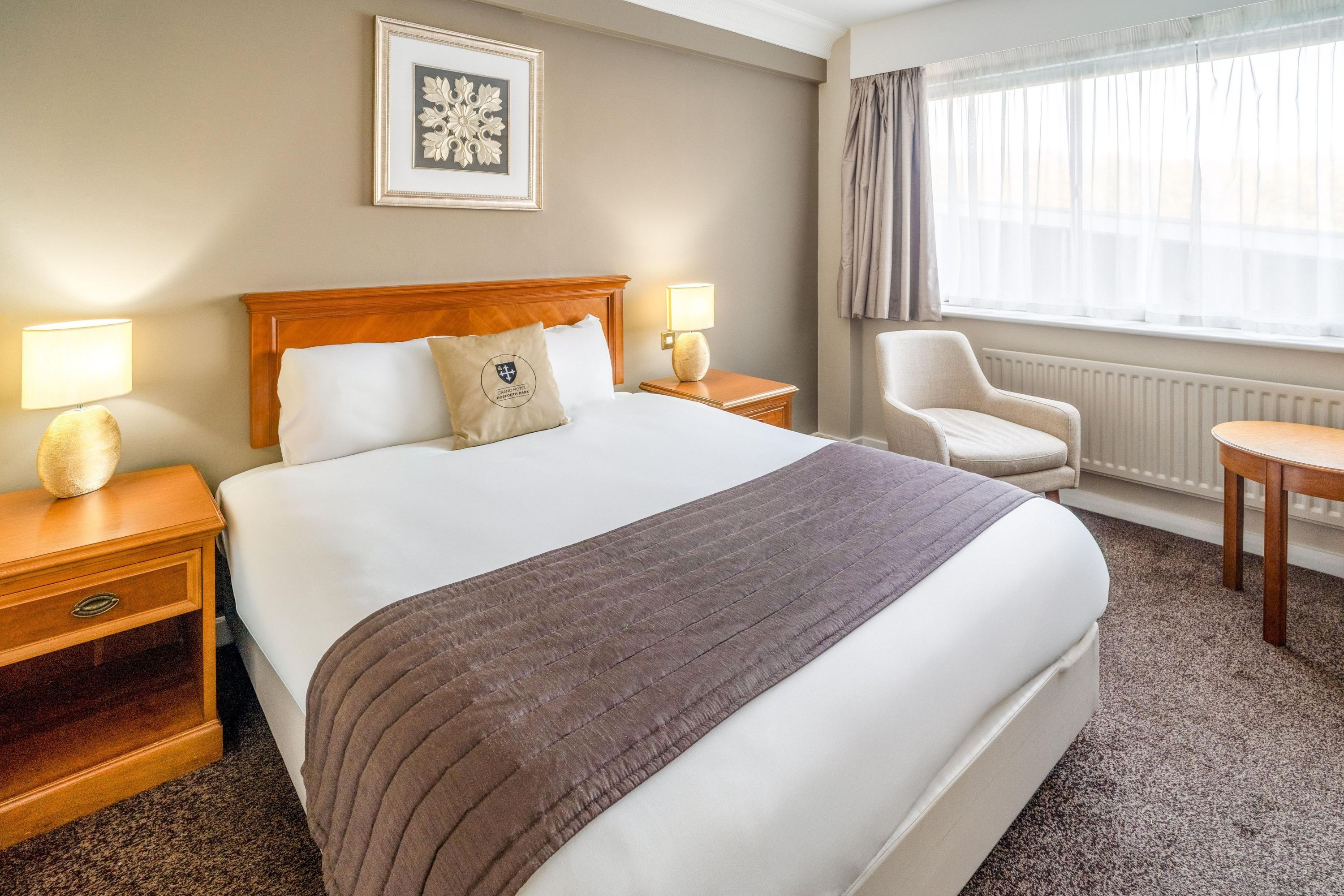 Habitación de hotel con una cama grande, dos mesitas de noche, una silla y un ventanal con cortinas.