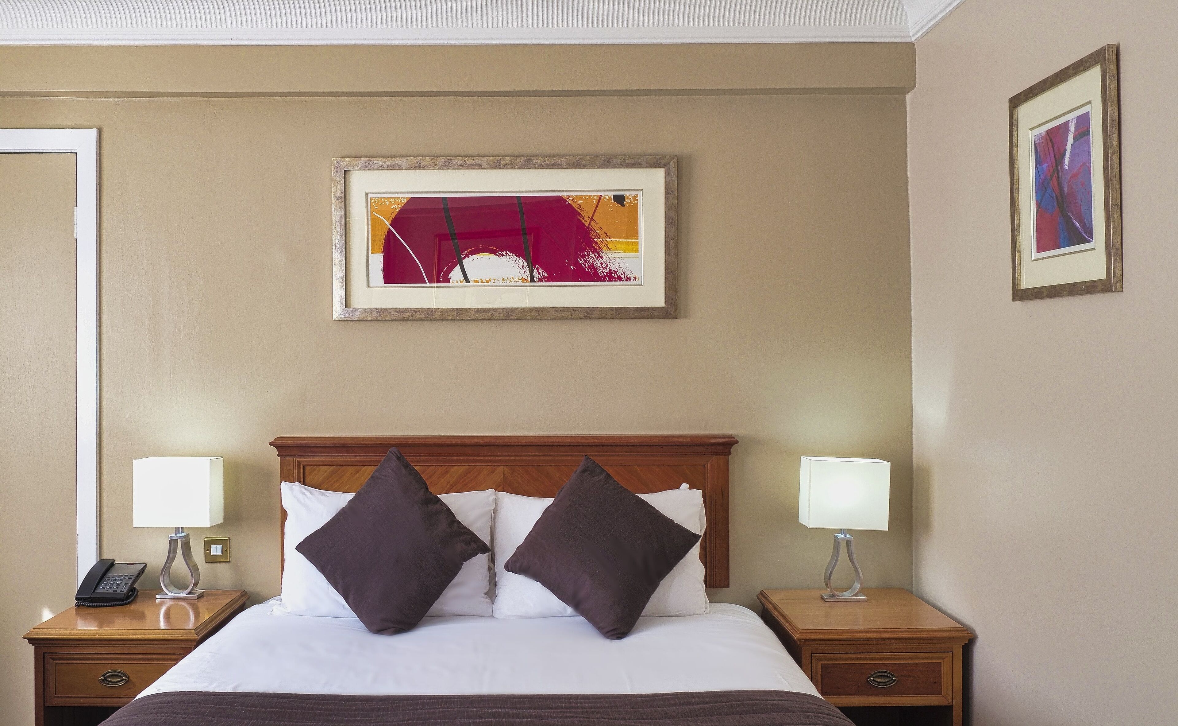 Una habitación de hotel con una cama grande, dos mesitas de noche, un cuadro abstracto enmarcado y otro cuadro en la pared.
