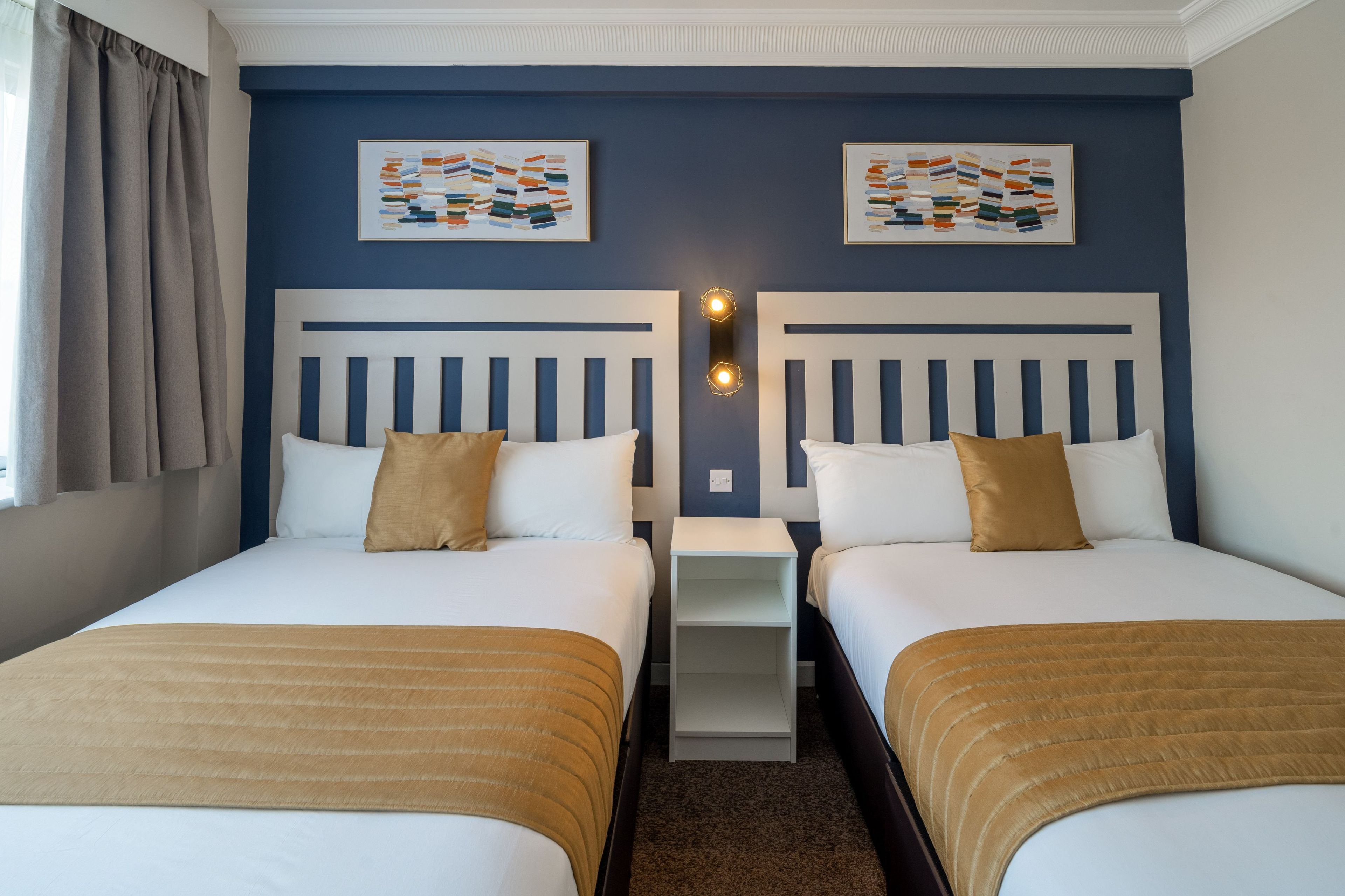 Een hotelkamer met twee bedden, een nachtkastje en kunstwerken aan de muur.