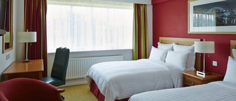 A hotel room with two beds, a desk, a chair, and a large window with curtains.