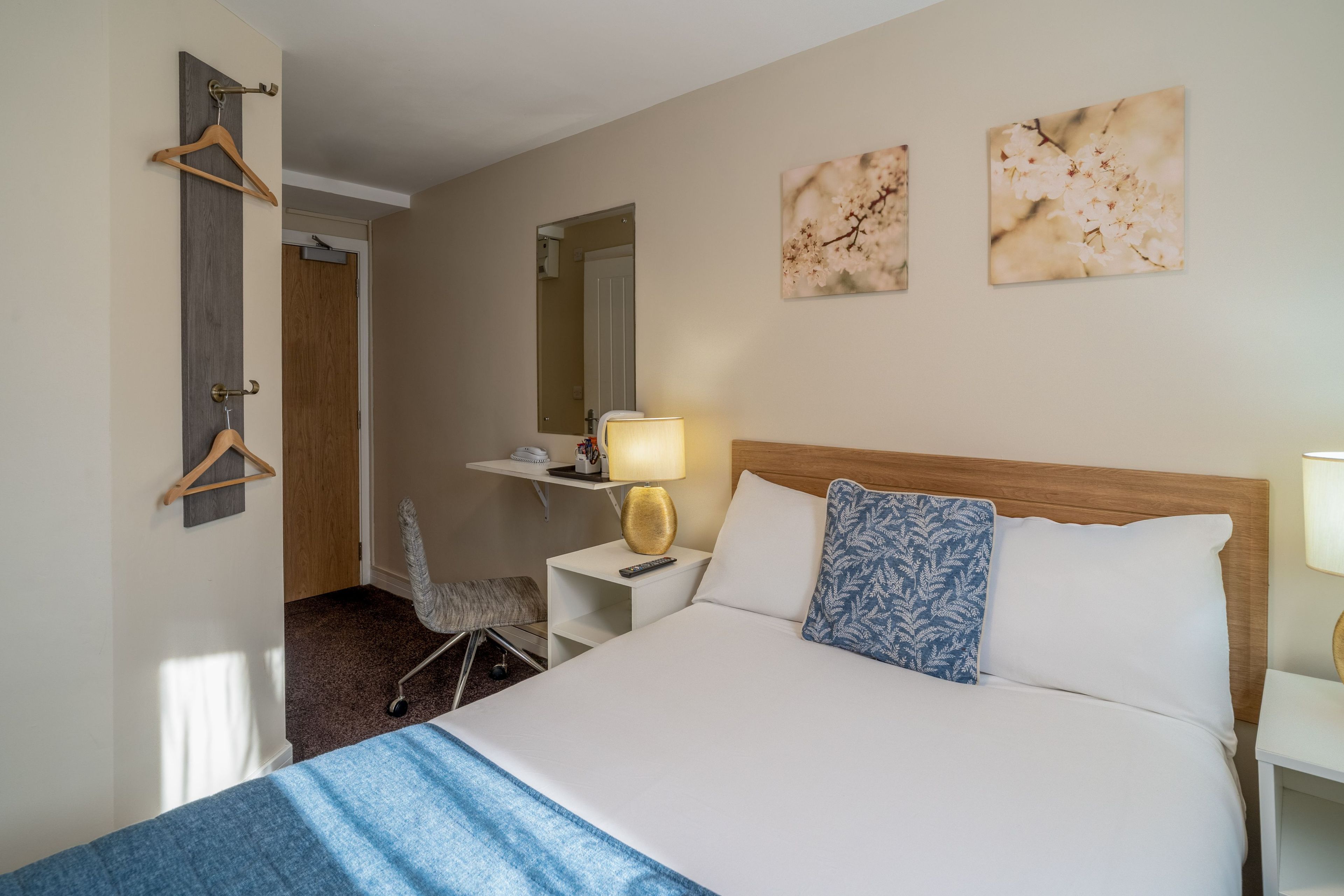 A hotel room with a bed, bedside table, lamp, and a chair.