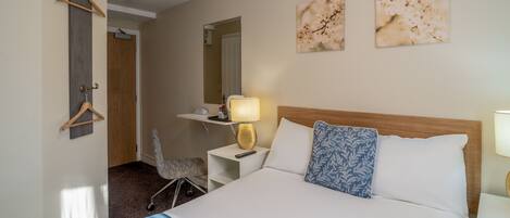 A hotel room with a bed, bedside table, lamp, and a chair.