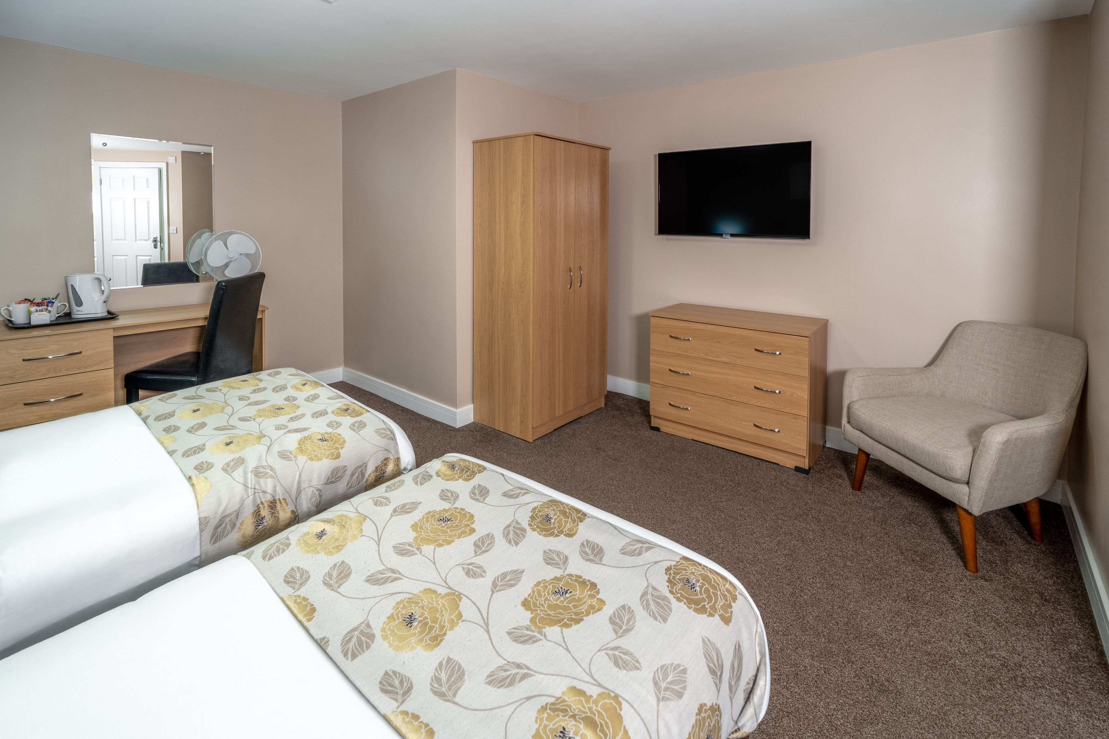A hotel room with two beds, a desk, a chair, a wardrobe, and a TV.
