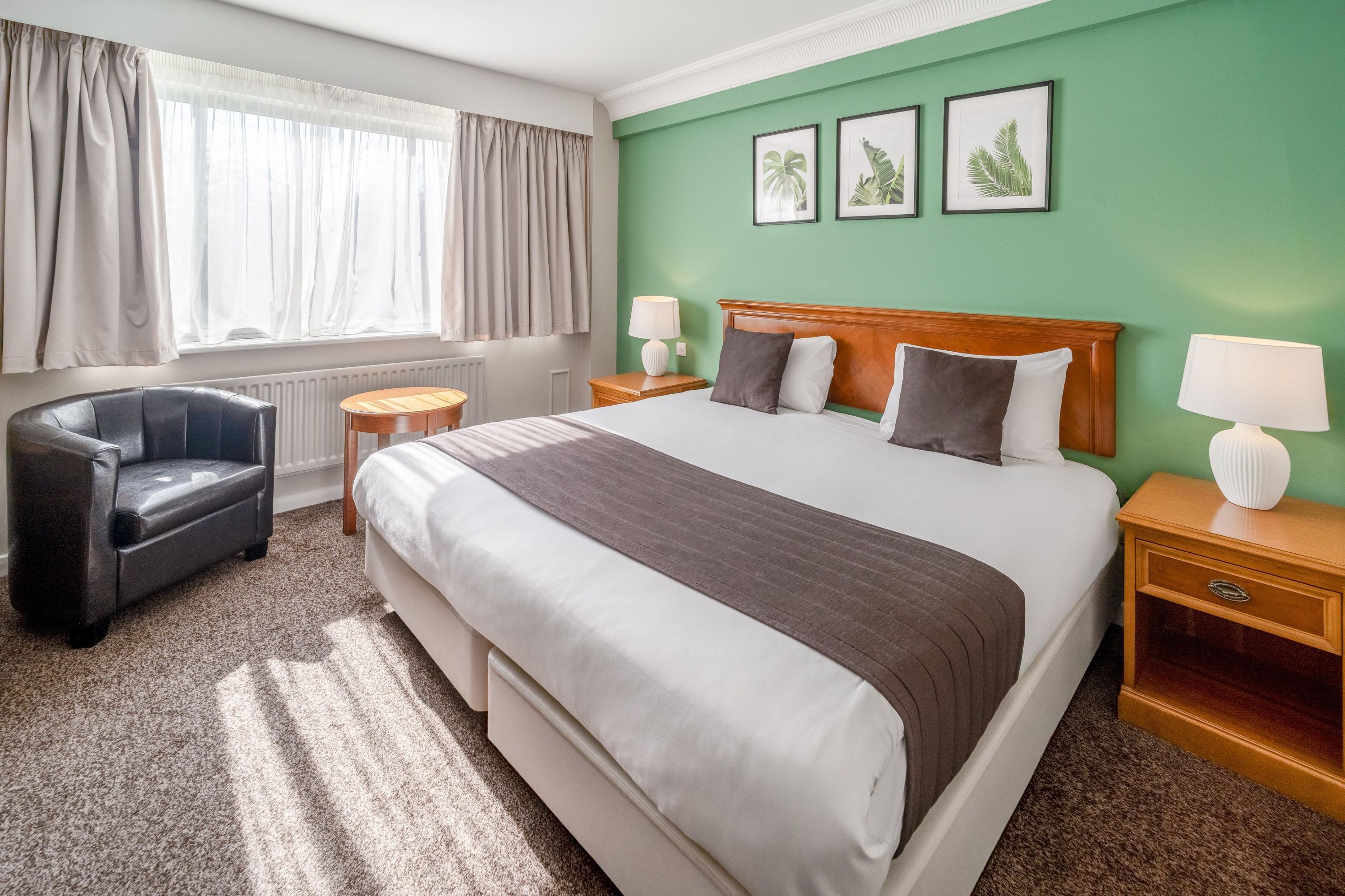 A hotel room with a large bed, a chair, a nightstand, a lamp, and a window with curtains.