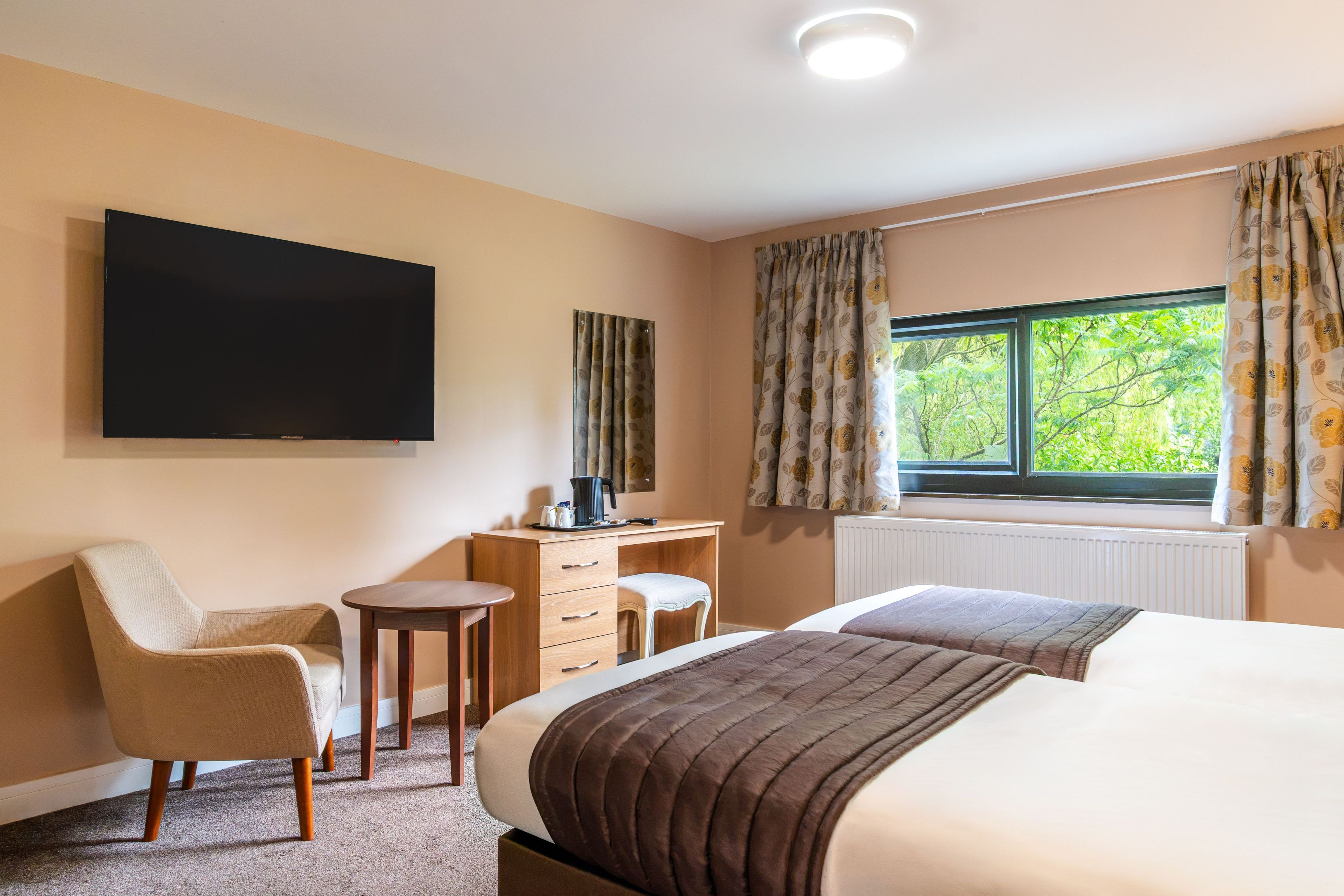 A hotel room with a bed, a desk, a chair, a television, and a window with curtains.