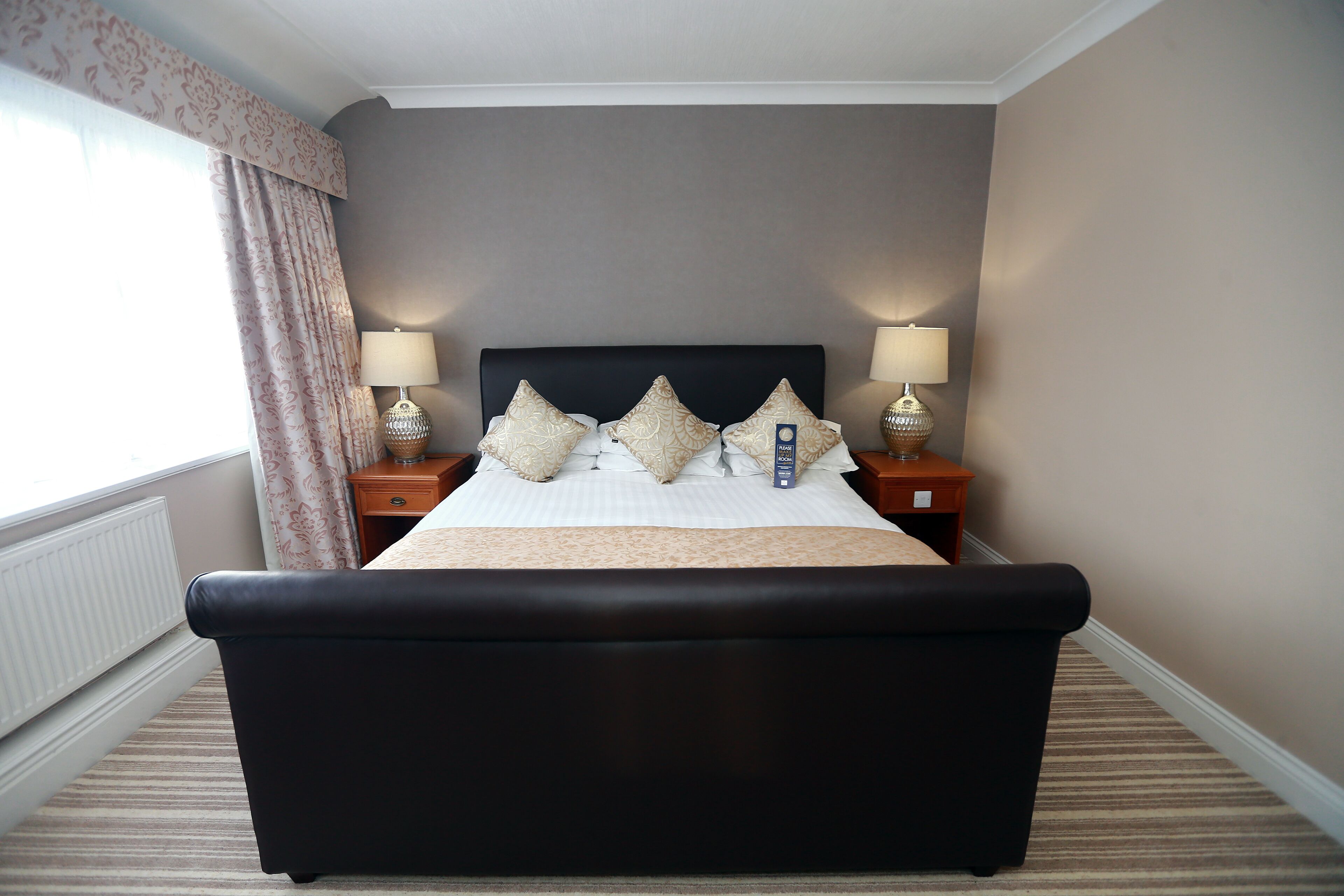 Een hotelkamer met een groot bed, twee nachtkastjes met lampen, een raam met gordijnen en een radiator.