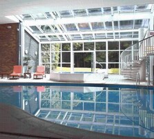 A swimming pool with a glass ceiling, a hot tub, and a staircase leading to an upper level.