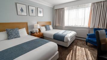 A hotel room with two beds, a desk, a chair, and a window with curtains.