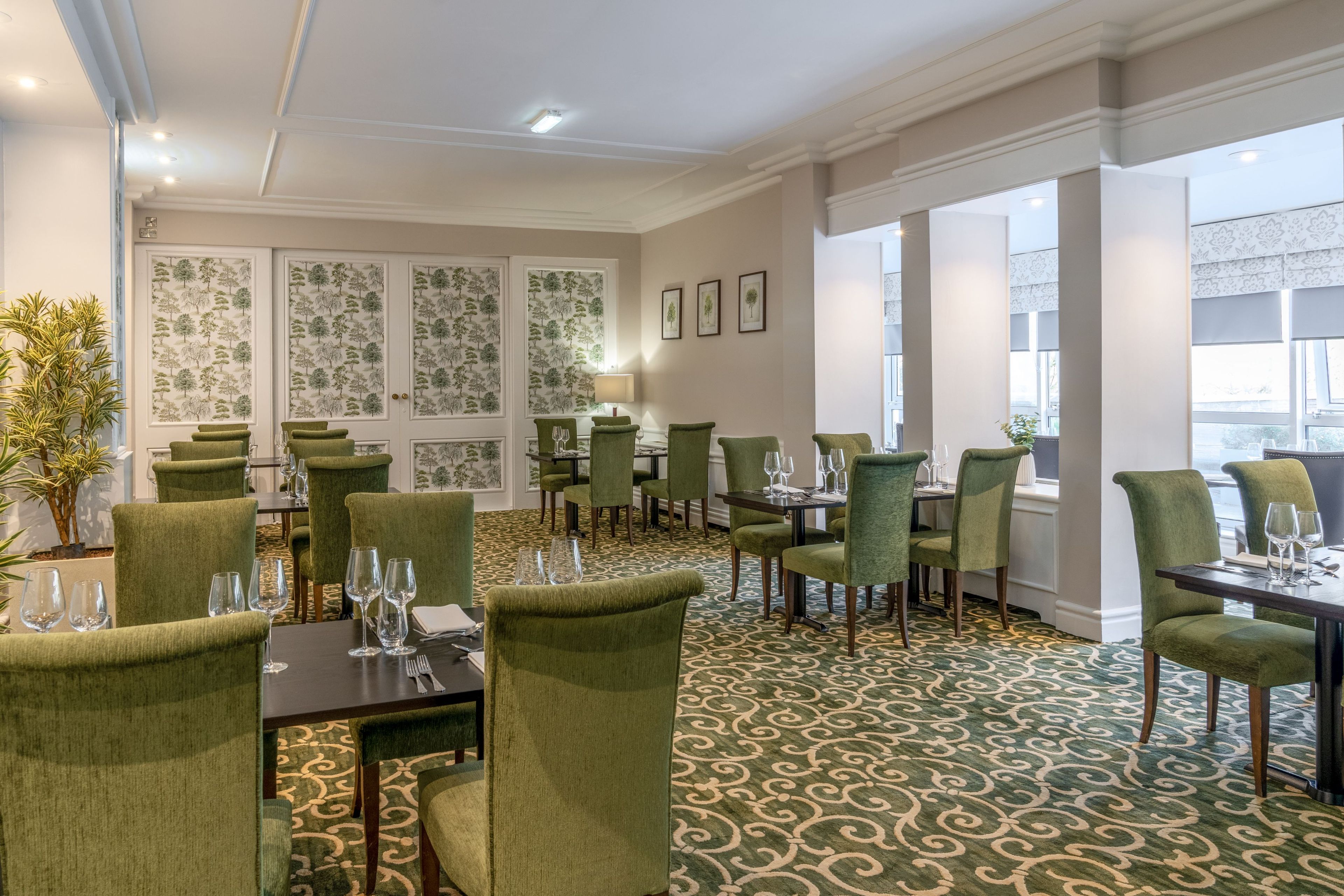 Een restaurantgedeelte in een hotel, met groen bekleden stoelen, gedekte tafels en een kamerbreed tapijt.