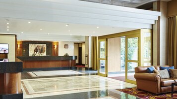 A hotel lobby with a reception desk, a large painting, a leather sofa, and a large window.