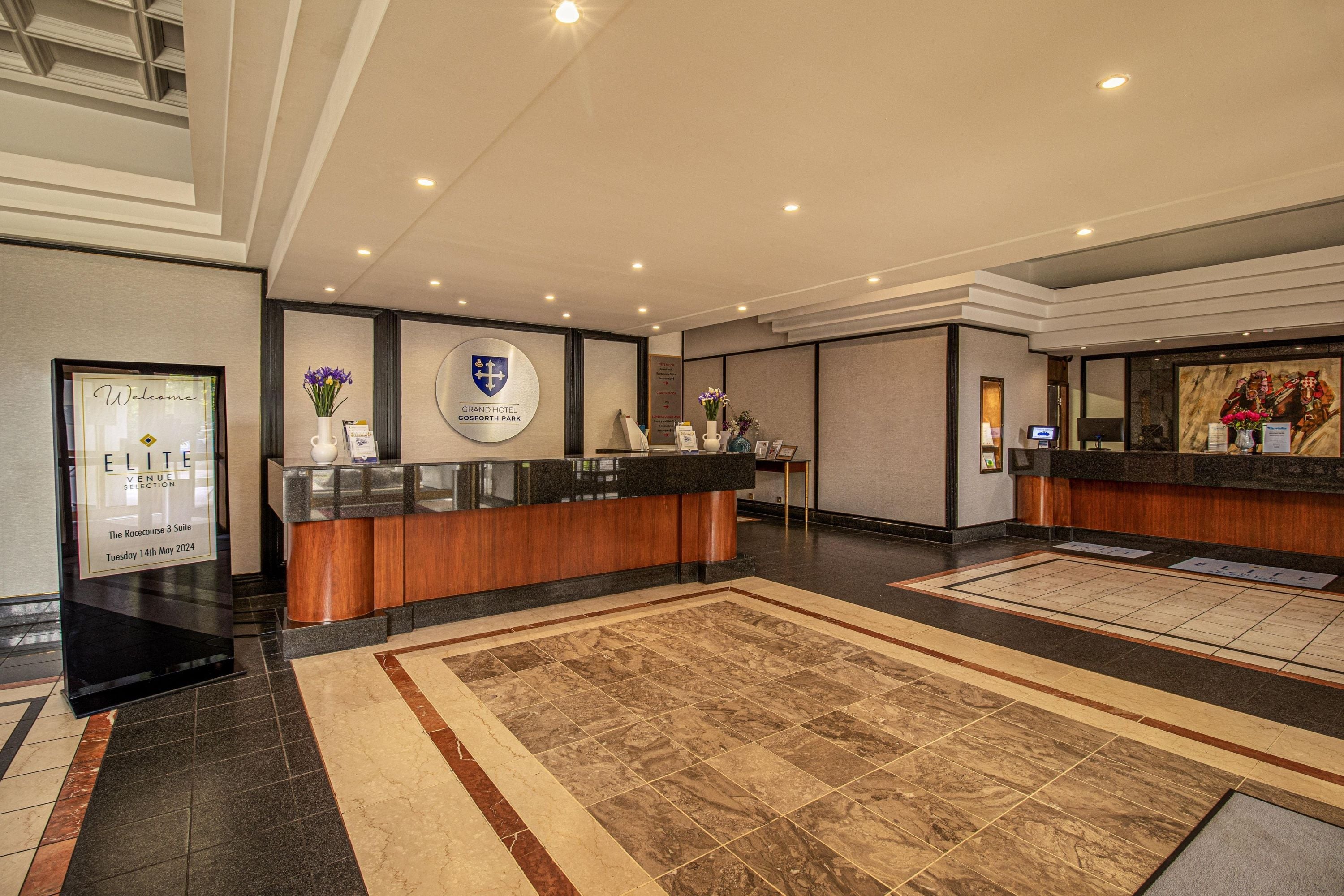 A hotel reception area with a reception desk, a large logo on the wall, and a carpeted floor.
