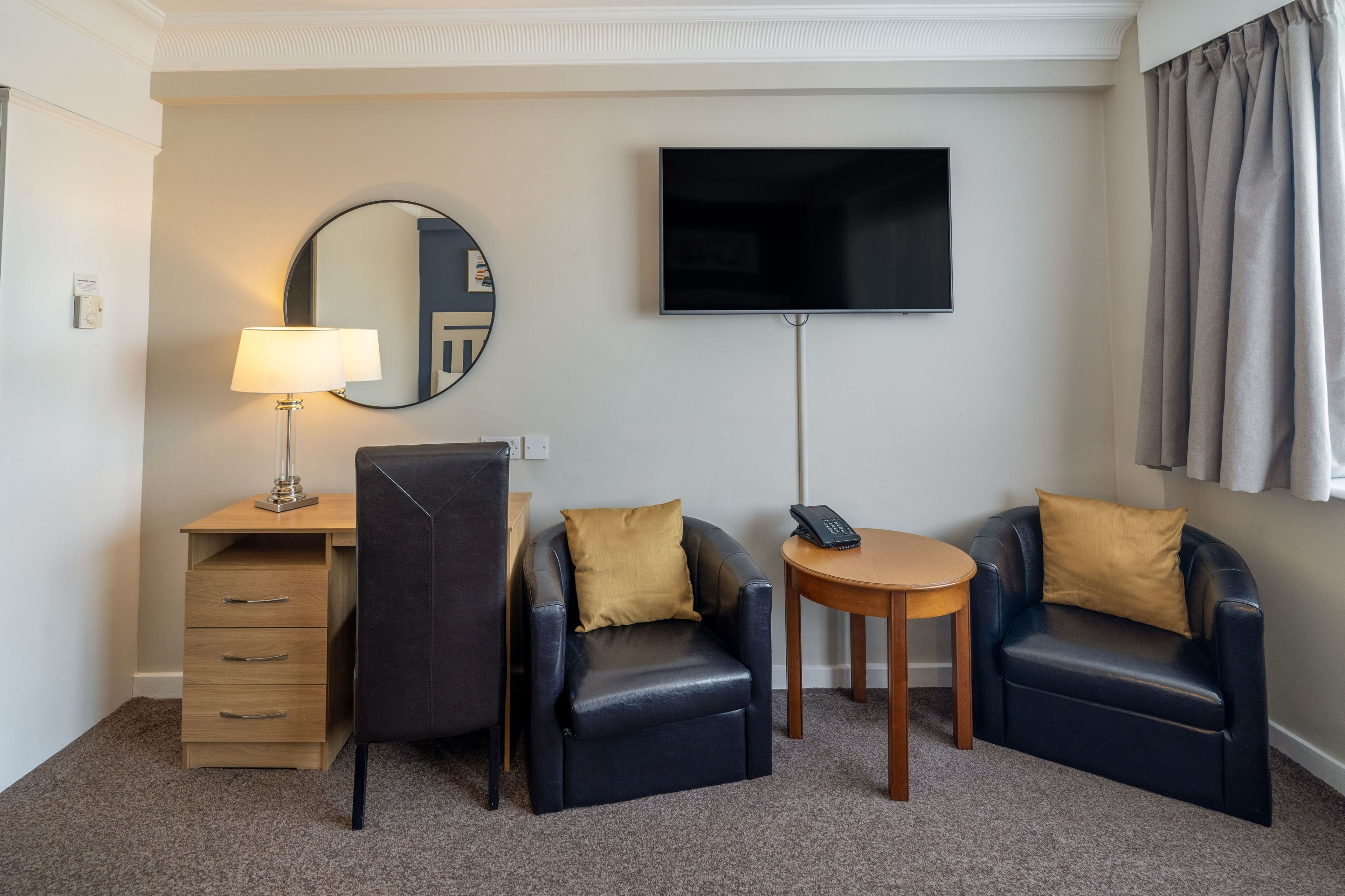 Een hotelkamer met een bureau, twee fauteuils, een televisie en een telefoon.