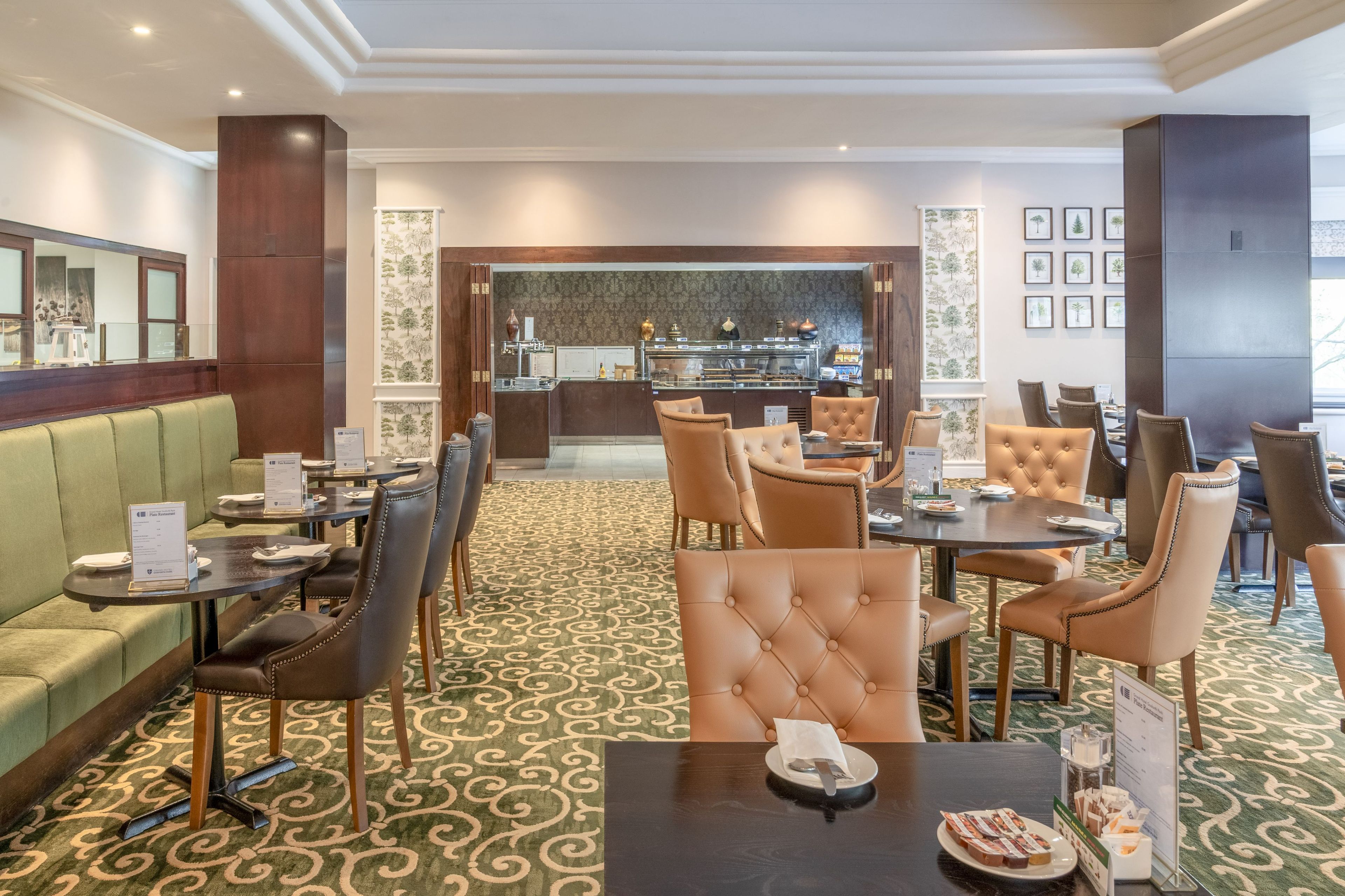 A hotel dining area with leather chairs, tables, and a green patterned carpet.