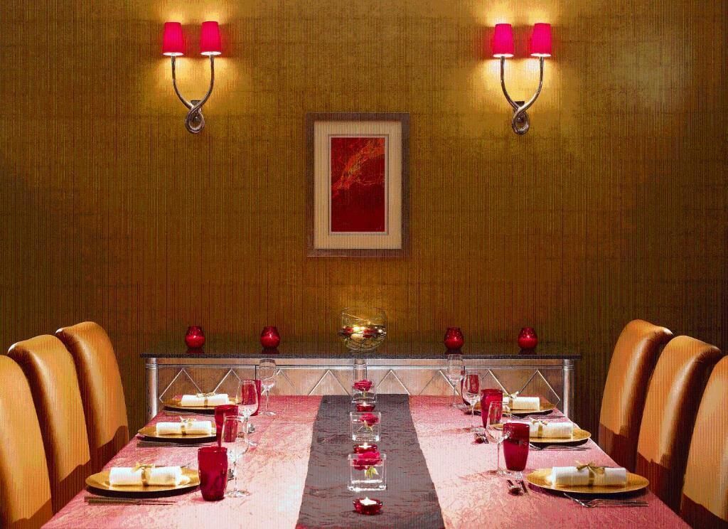 A dining room with a long table set for a meal, two wall-mounted lamps, and a framed artwork on the wall.
