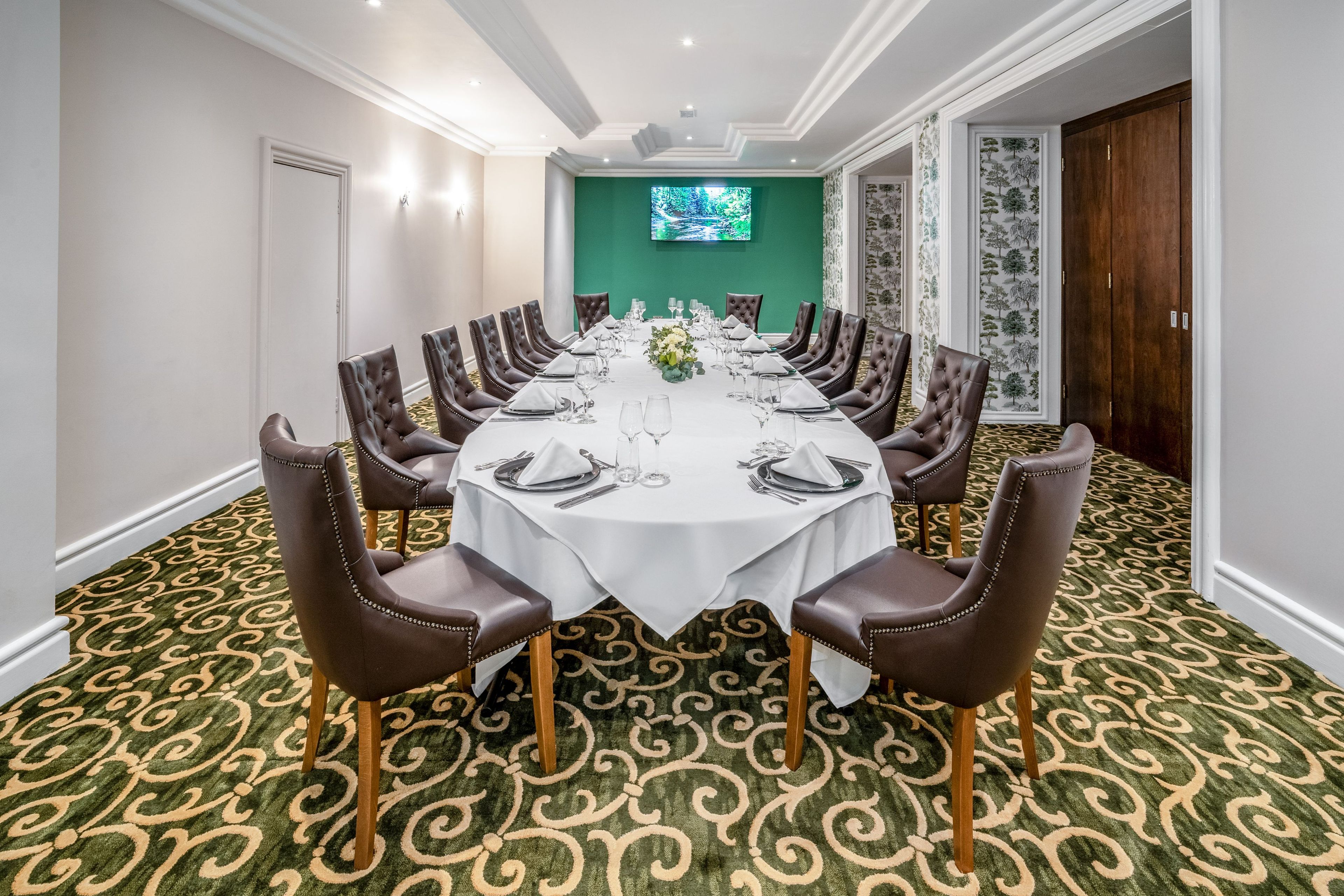 A conference room with a long table set for a meeting, surrounded by leather chairs.