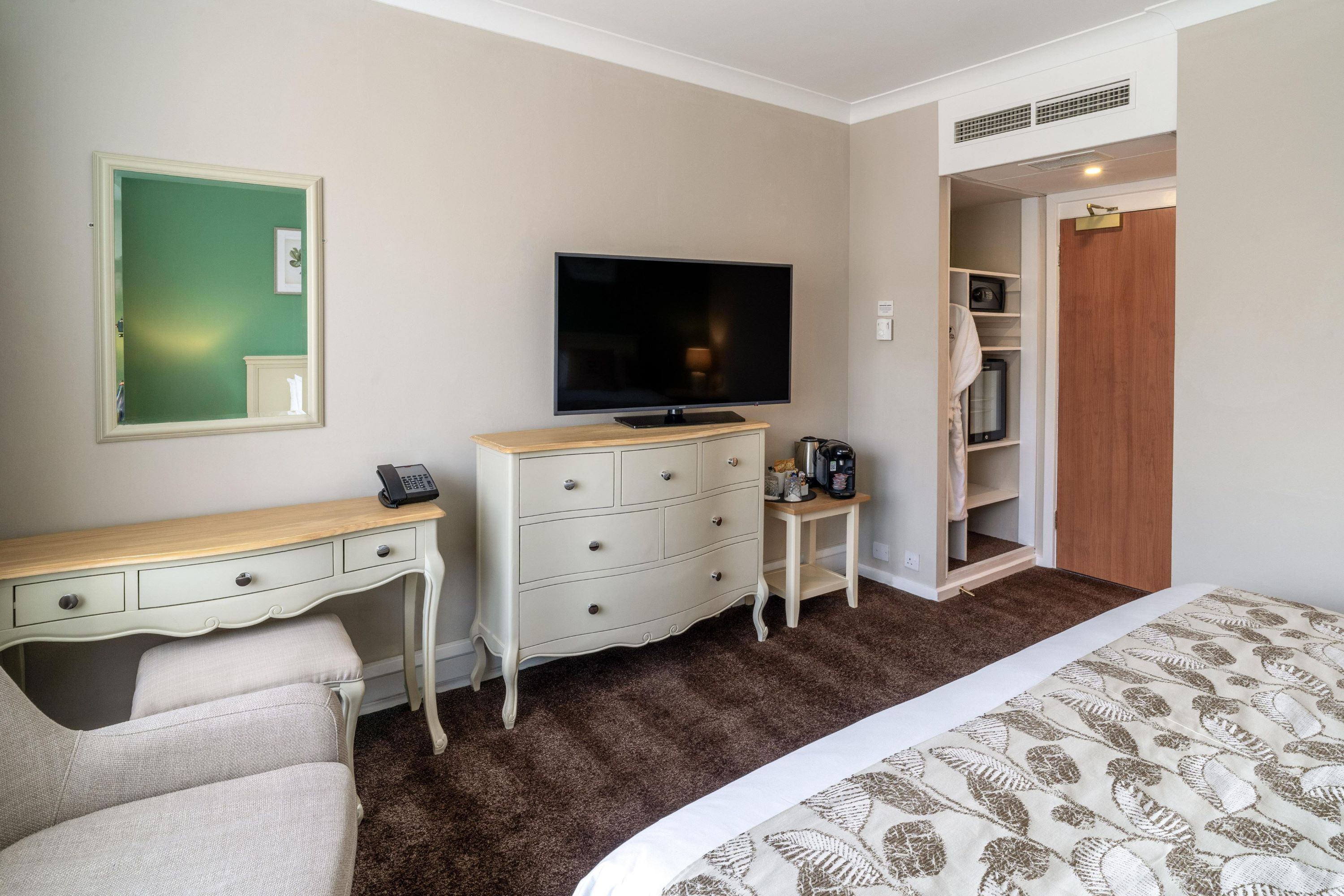 A hotel room with a bed, a desk, a dresser, a television, a closet, and a bathroom.