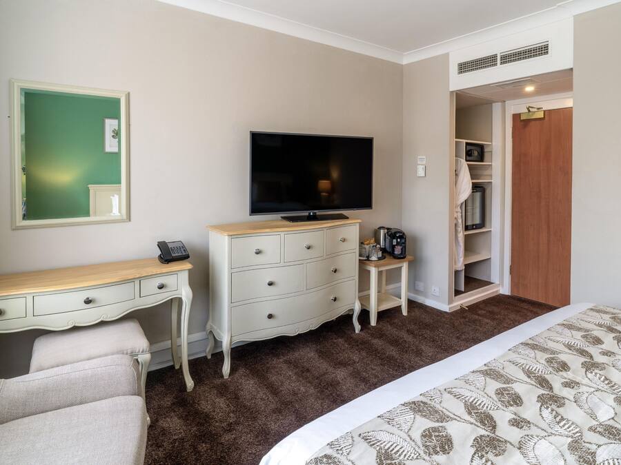 Quarto de hotel com cama, escrivaninha, cômoda, televisão, armário e banheiro.