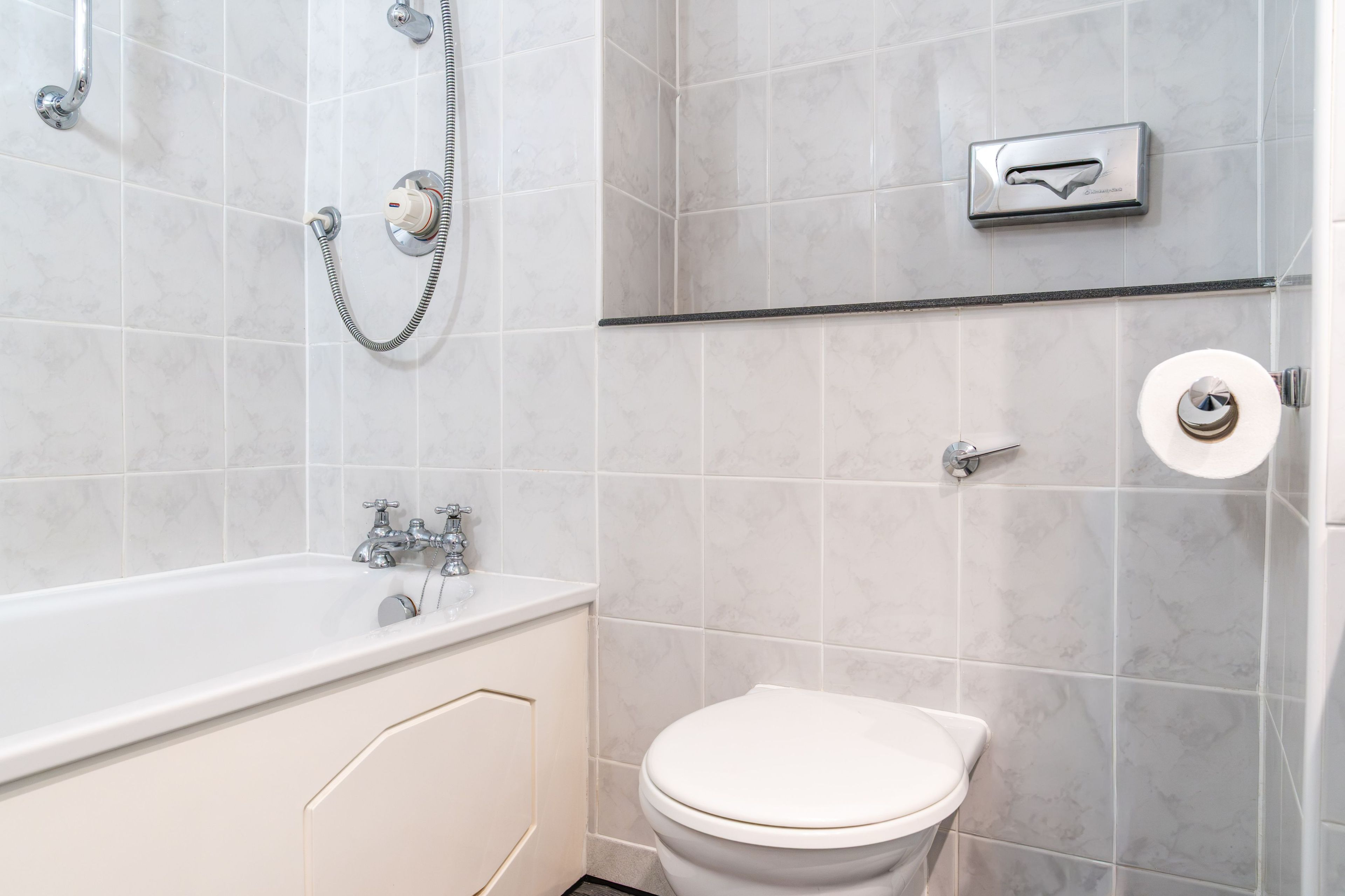 A bathroom with a bathtub, toilet, and a shower with a handheld showerhead.