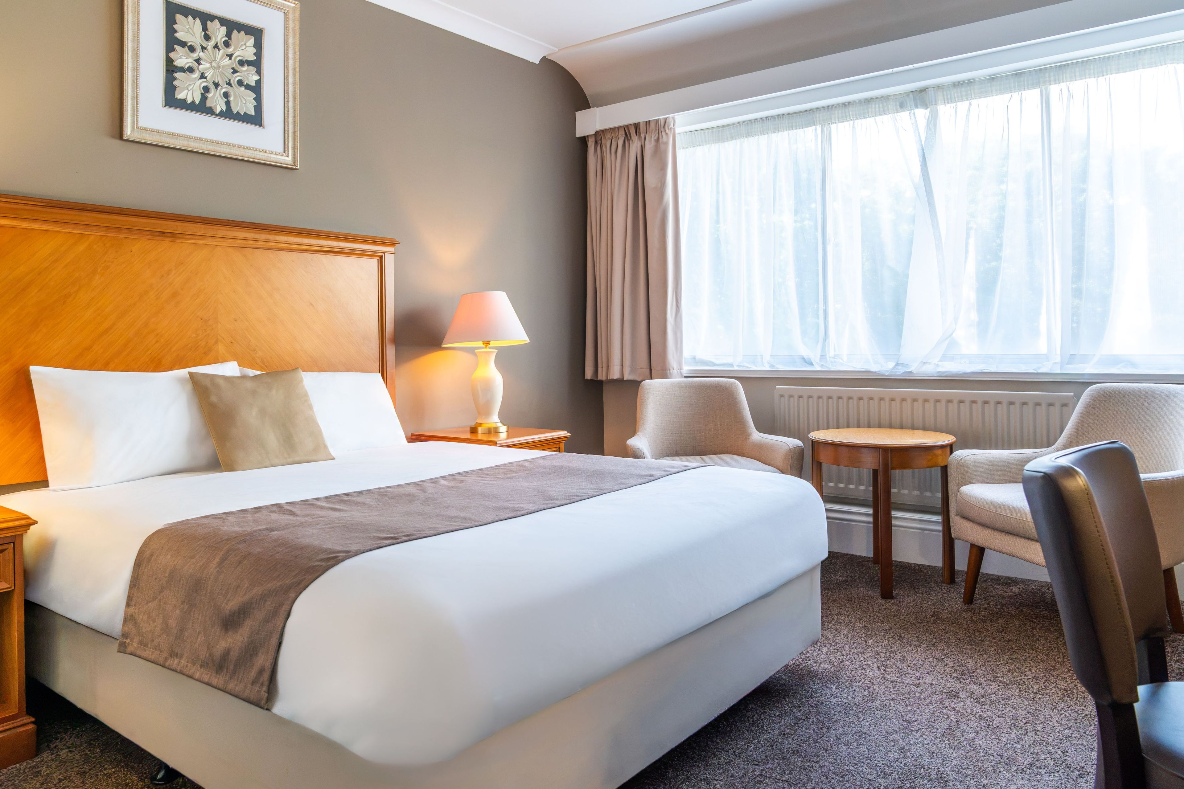 Une chambre d’hôtel avec un grand lit, une table de chevet, une lampe, une chaise et une fenêtre avec des rideaux.