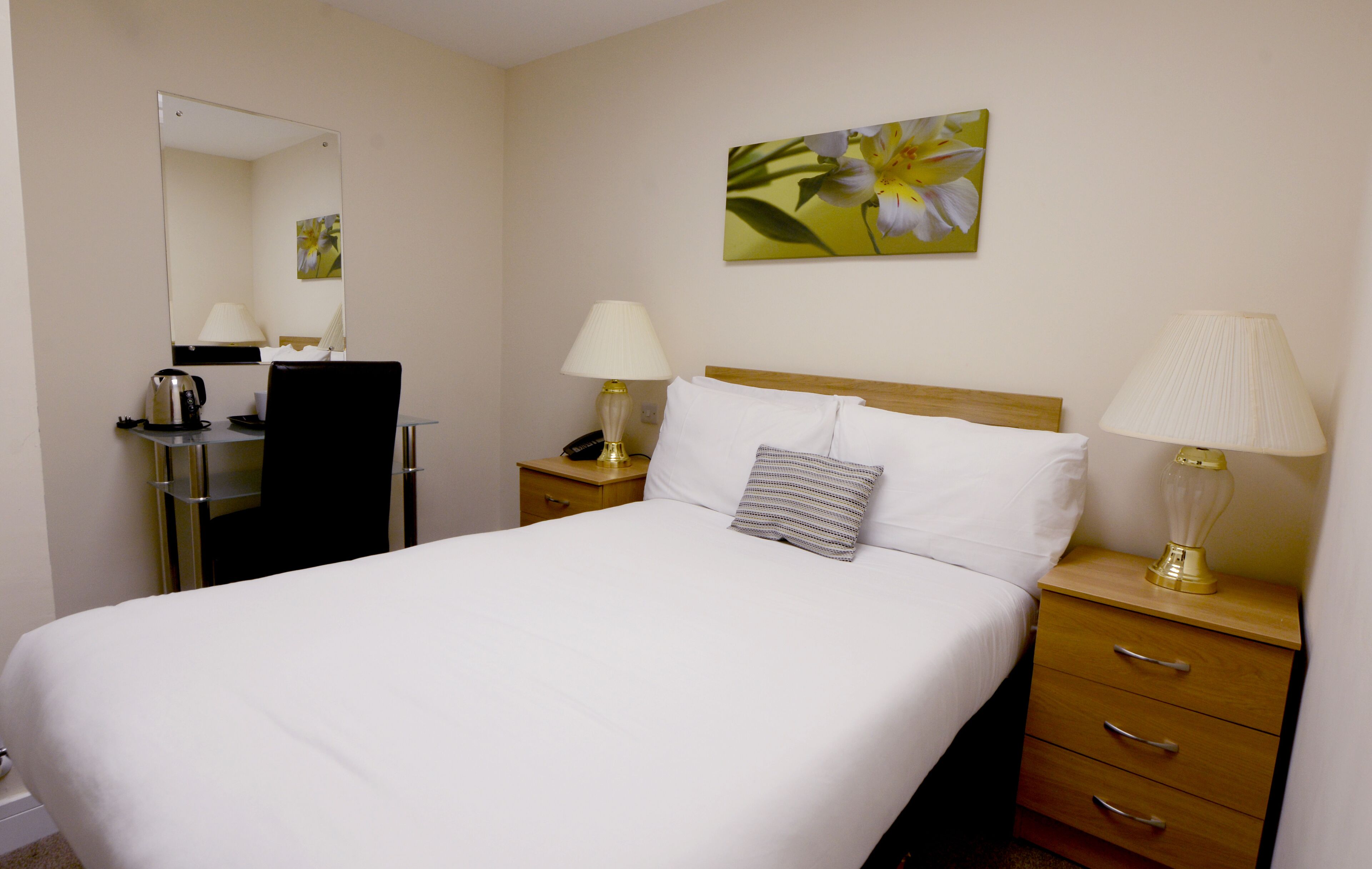 A hotel room with a bed, bedside tables, lamps, a mirror, a painting, and a coffee maker.