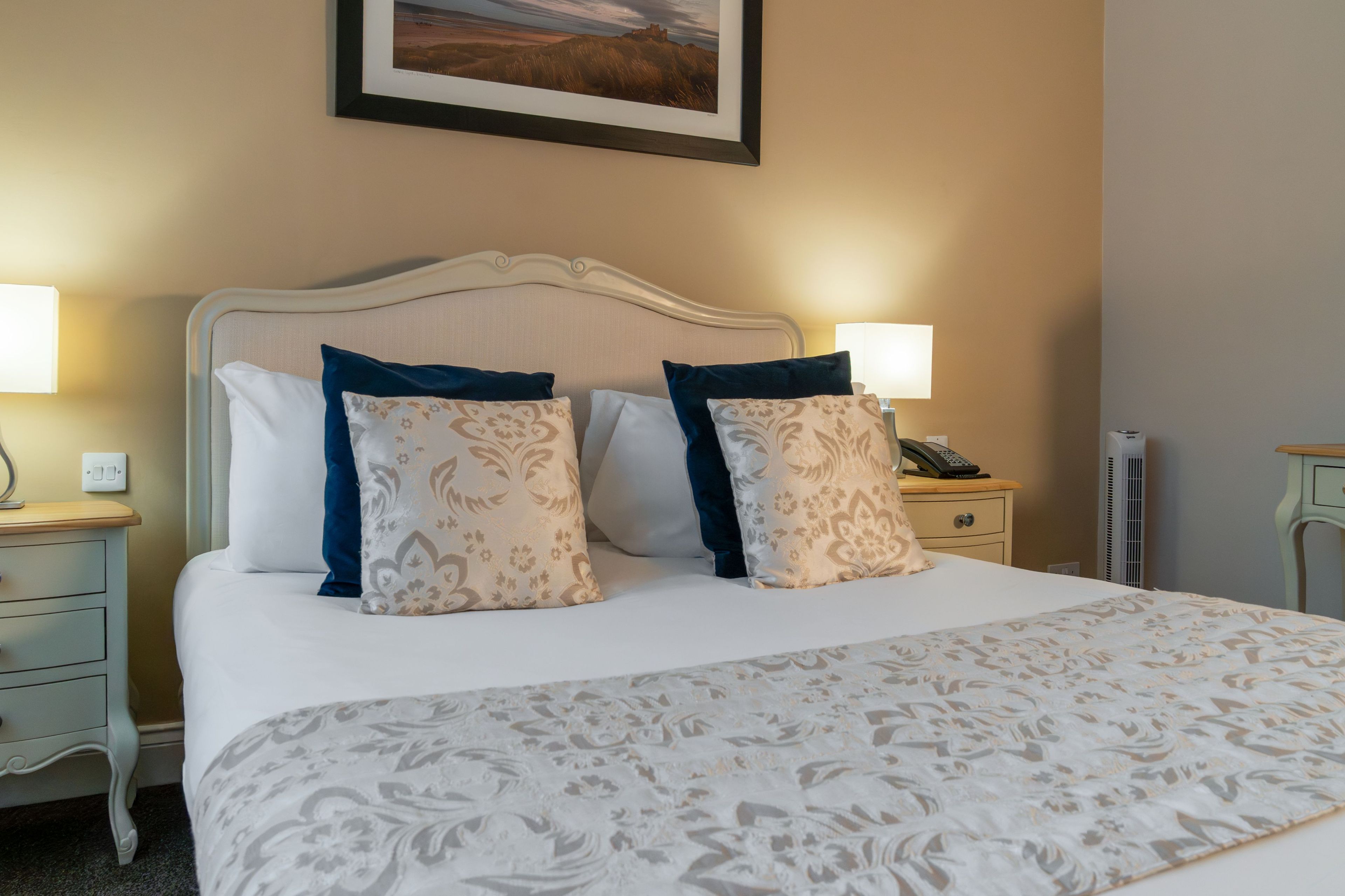 A neatly made bed with patterned bedding, two bedside tables with lamps, and a framed picture on the wall.