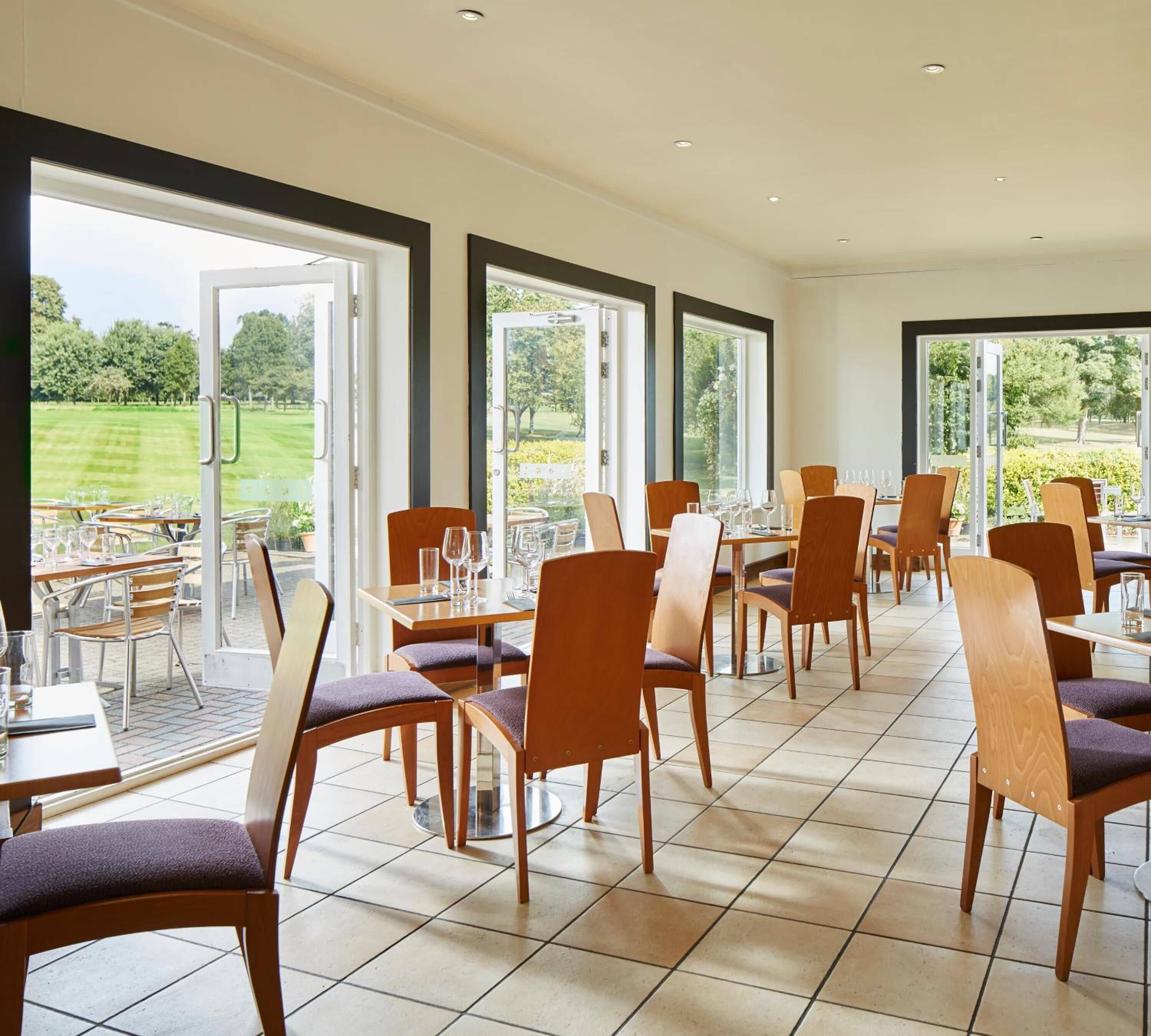 A restaurant with outdoor seating, large windows, and a view of a golf course.