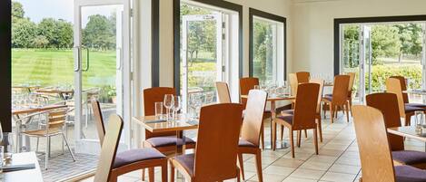Un restaurante con terraza, amplios ventanales y vistas a un campo de golf.