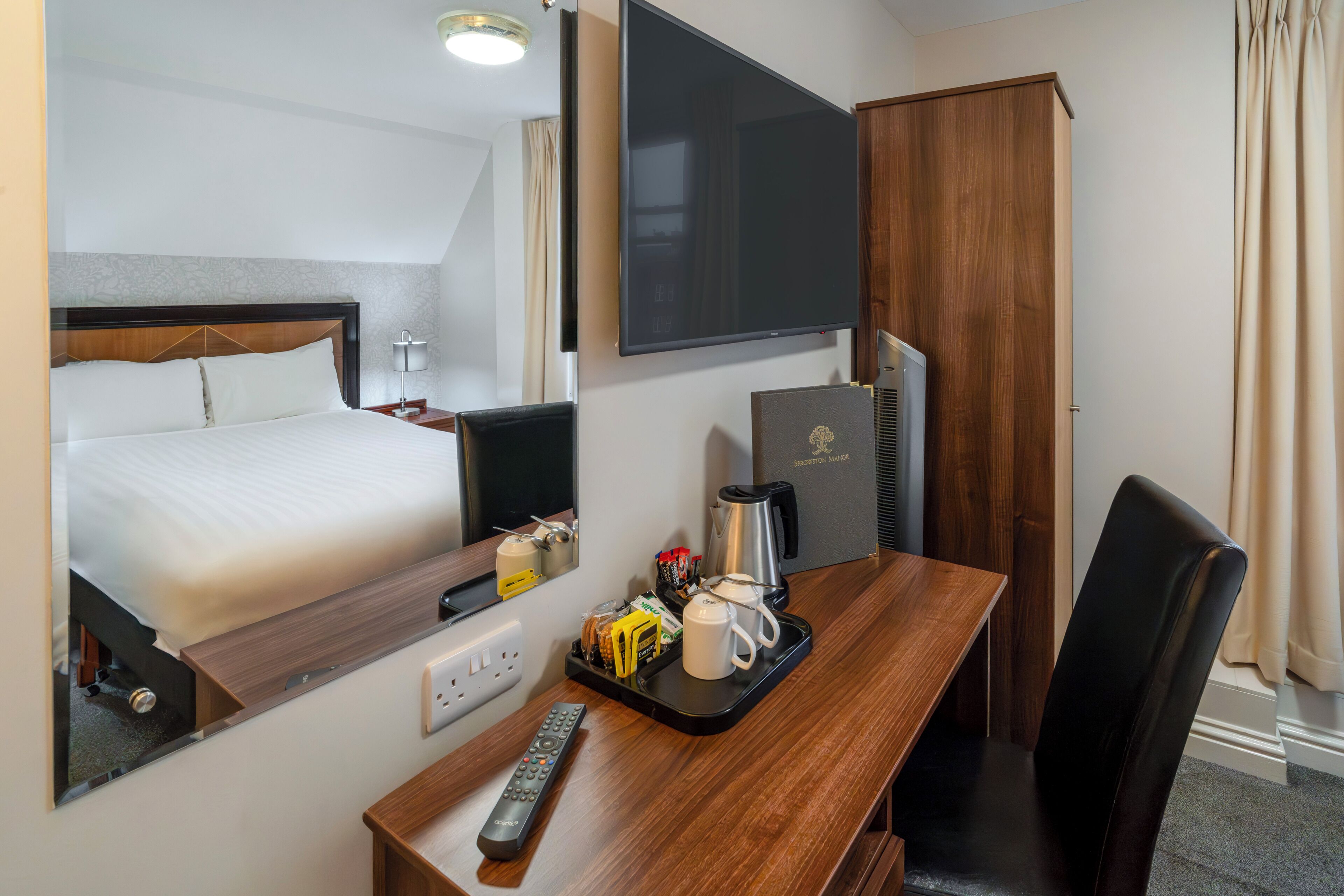 Une chambre d’hôtel équipée d’un lit, d’un bureau avec une machine à café, d’une télécommande et d’un téléviseur.