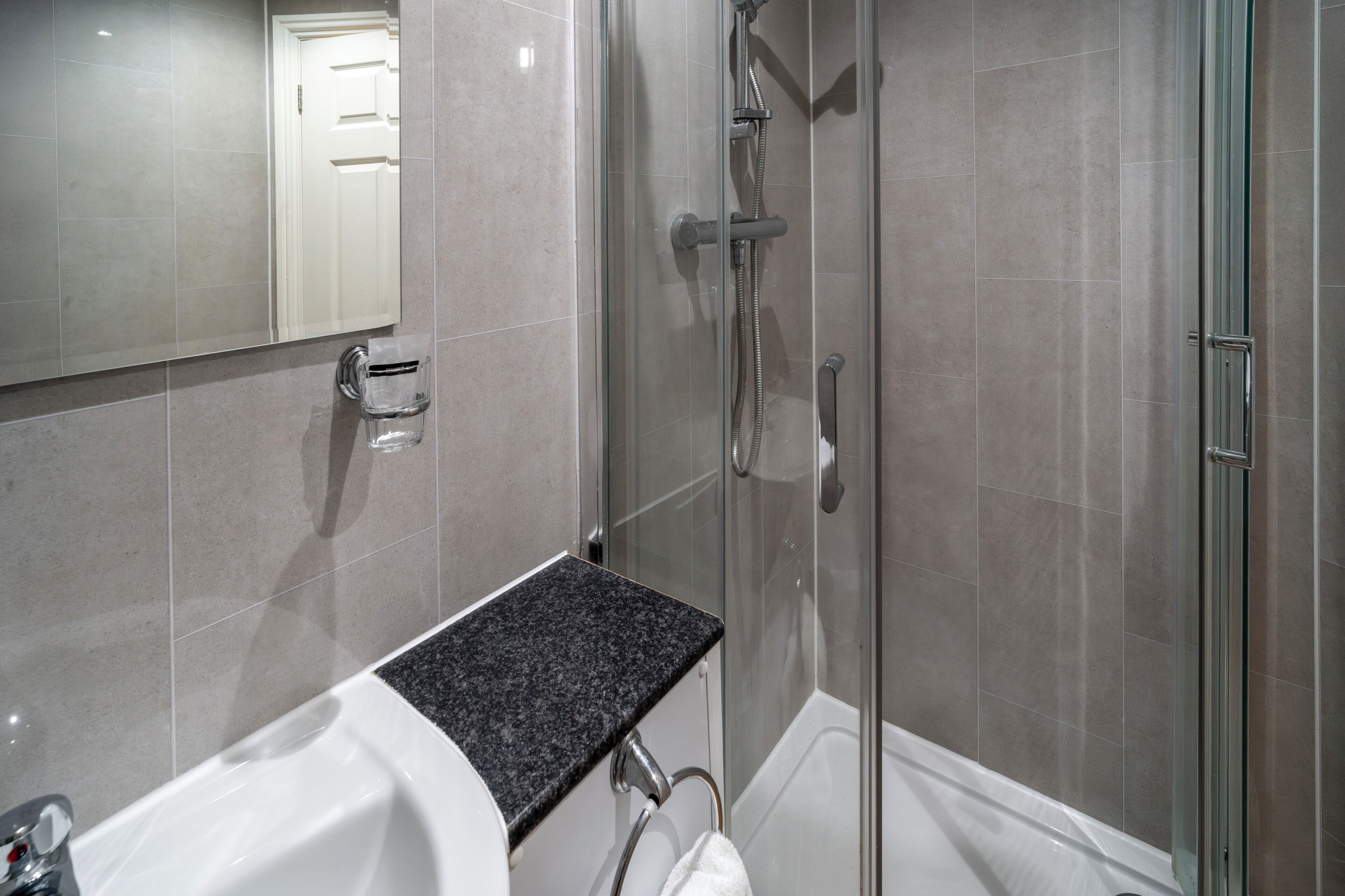A modern bathroom with a glass shower enclosure, a white bathtub, and a granite countertop.