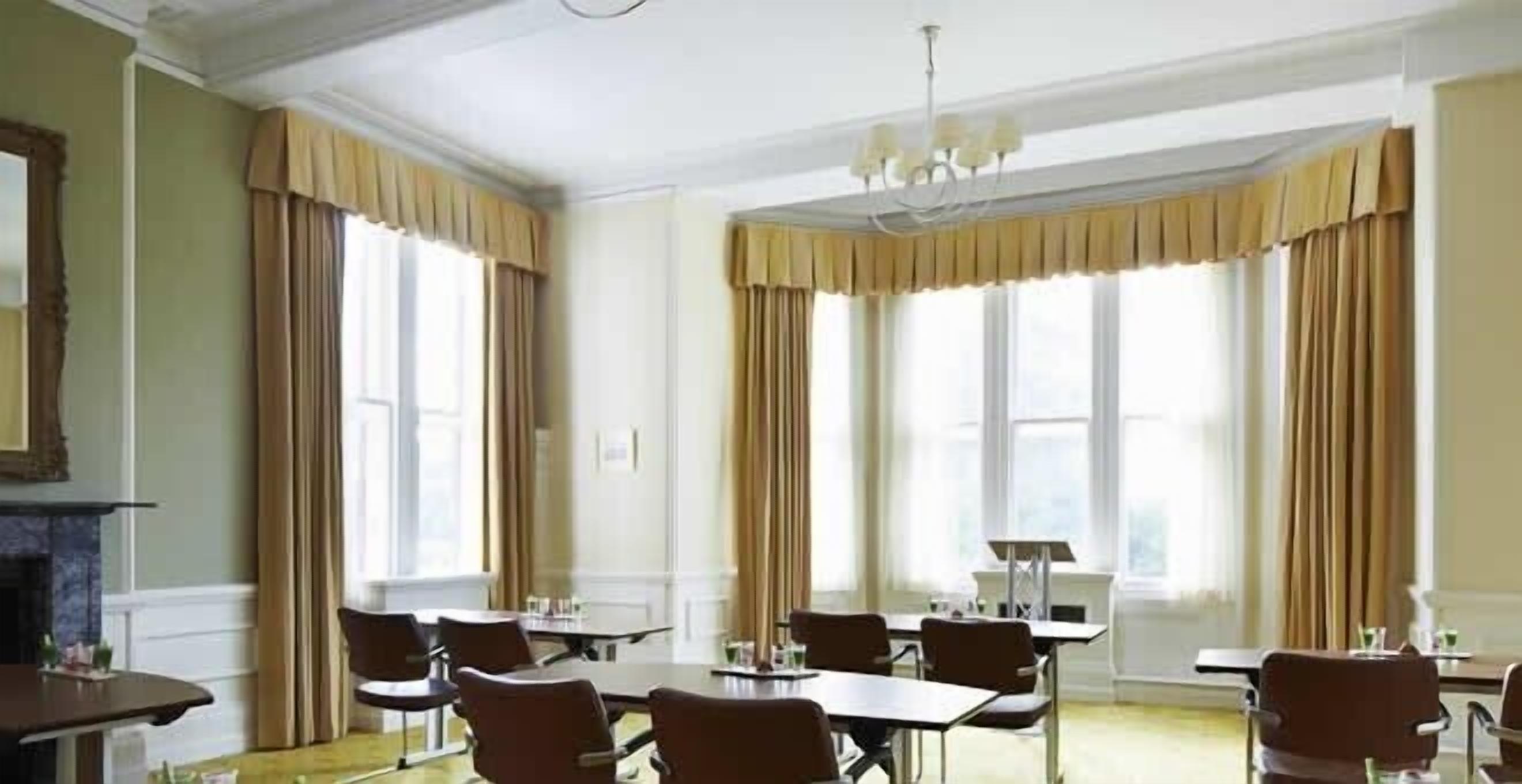 A conference room with tables and chairs, large windows with curtains, and a chandelier.