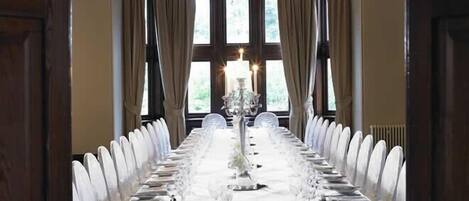 Una larga mesa de comedor dispuesta con vajilla blanca y sillas, con una araña en el centro.