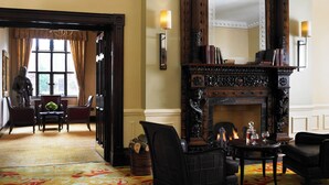 A room with a fireplace, a large mirror, and a view of a garden through a window. - Sprowston Manor Hotel, Spa & Golf (Norwich)