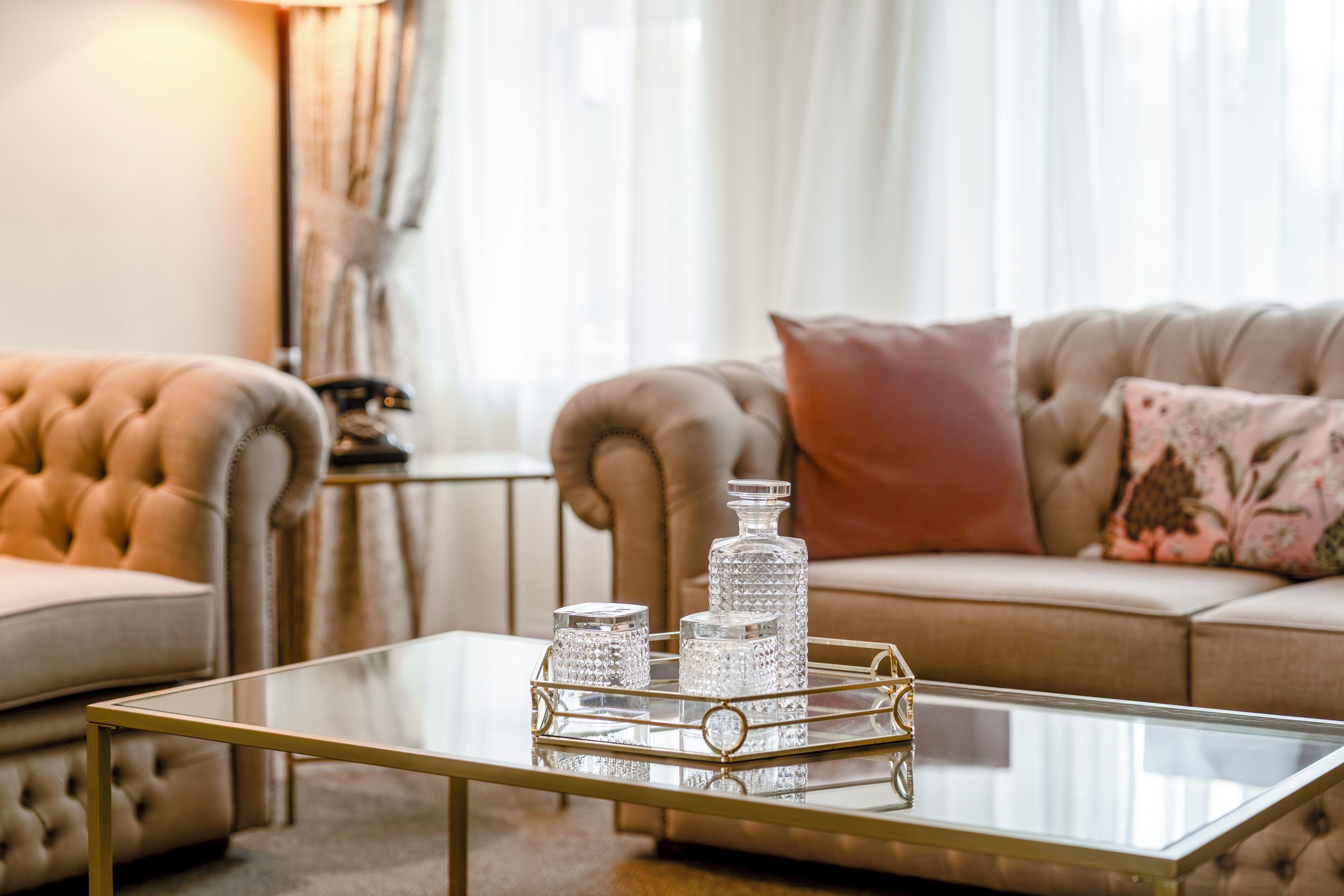 A living room with a glass coffee table, two armchairs, a sofa, and decorative glassware.