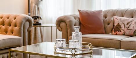 A living room with a glass coffee table, two armchairs, a sofa, and decorative glassware.
