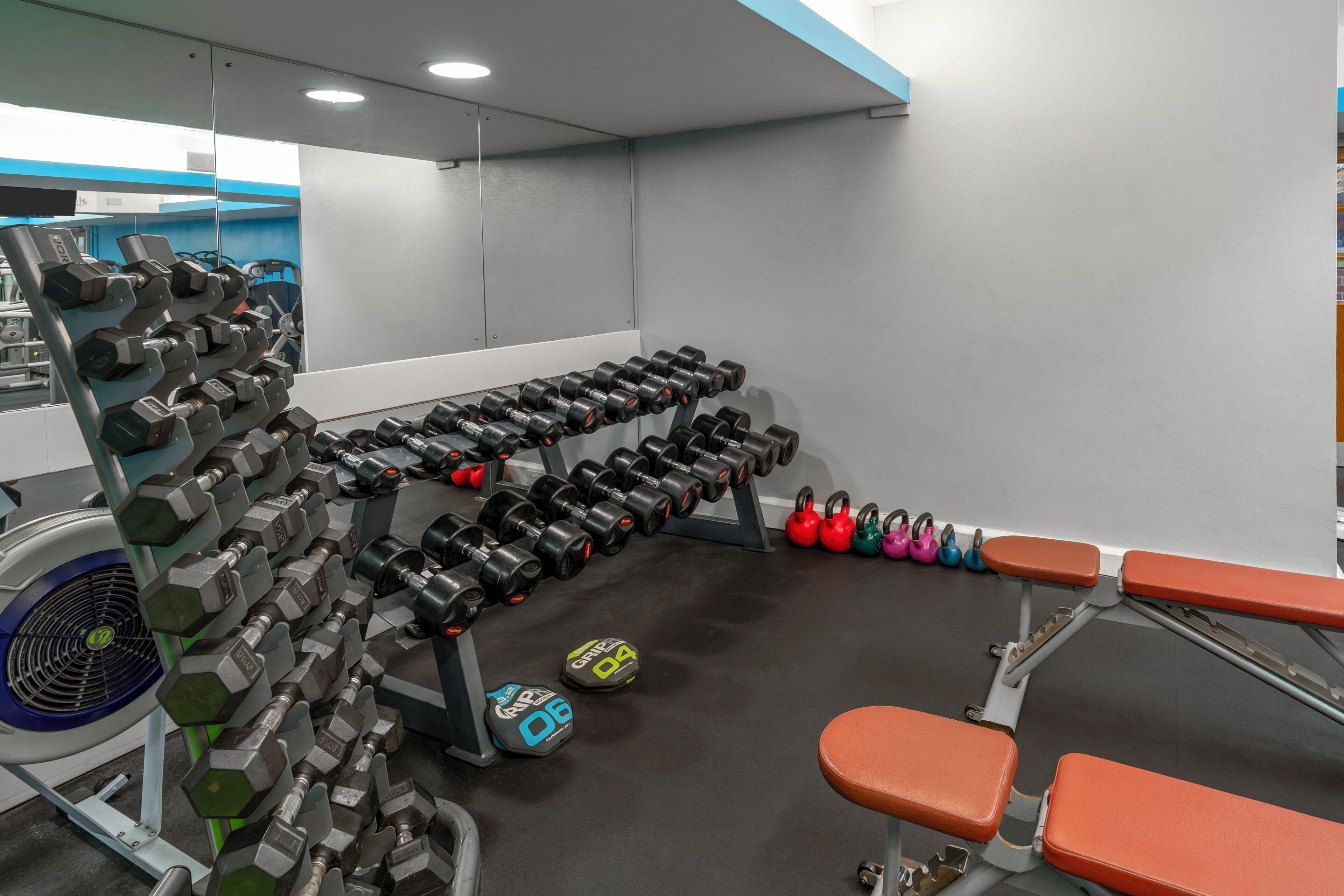 Un gimnasio con racks de pesas, mancuernas, kettlebells y equipo de ejercicio.