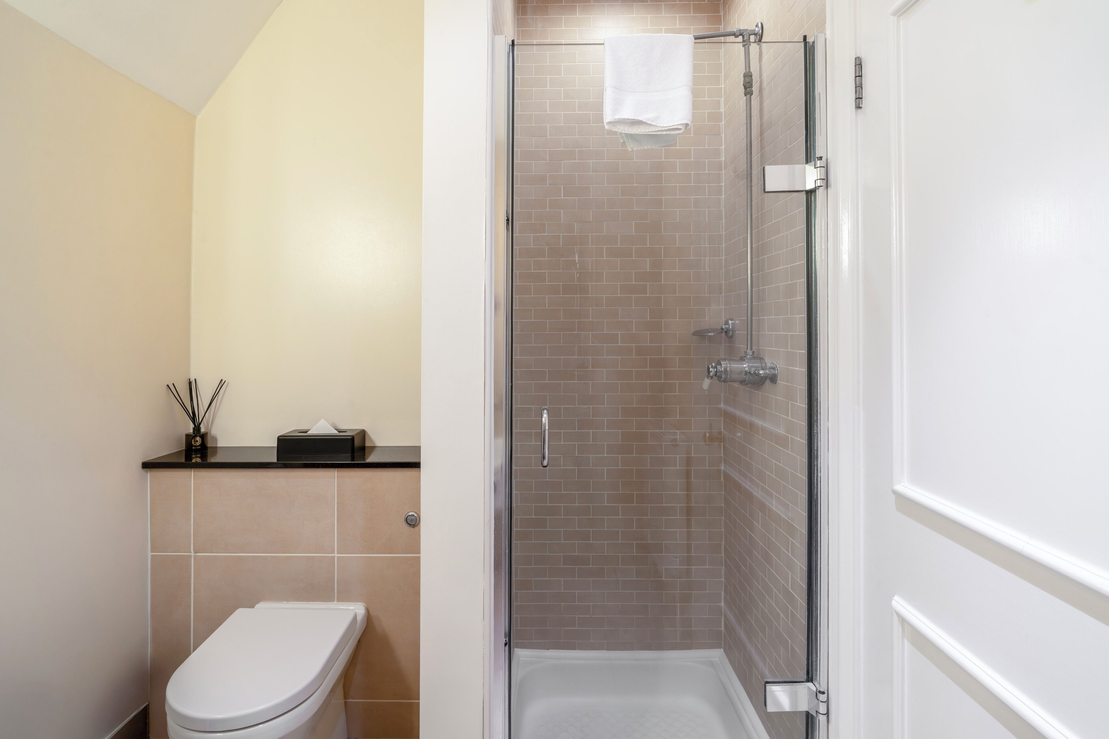 Un baño con inodoro, ducha con puerta de cristal y toalla colgada en la puerta de la ducha.