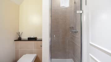 Un baño con inodoro, ducha con puerta de cristal y toalla colgada en la puerta de la ducha.