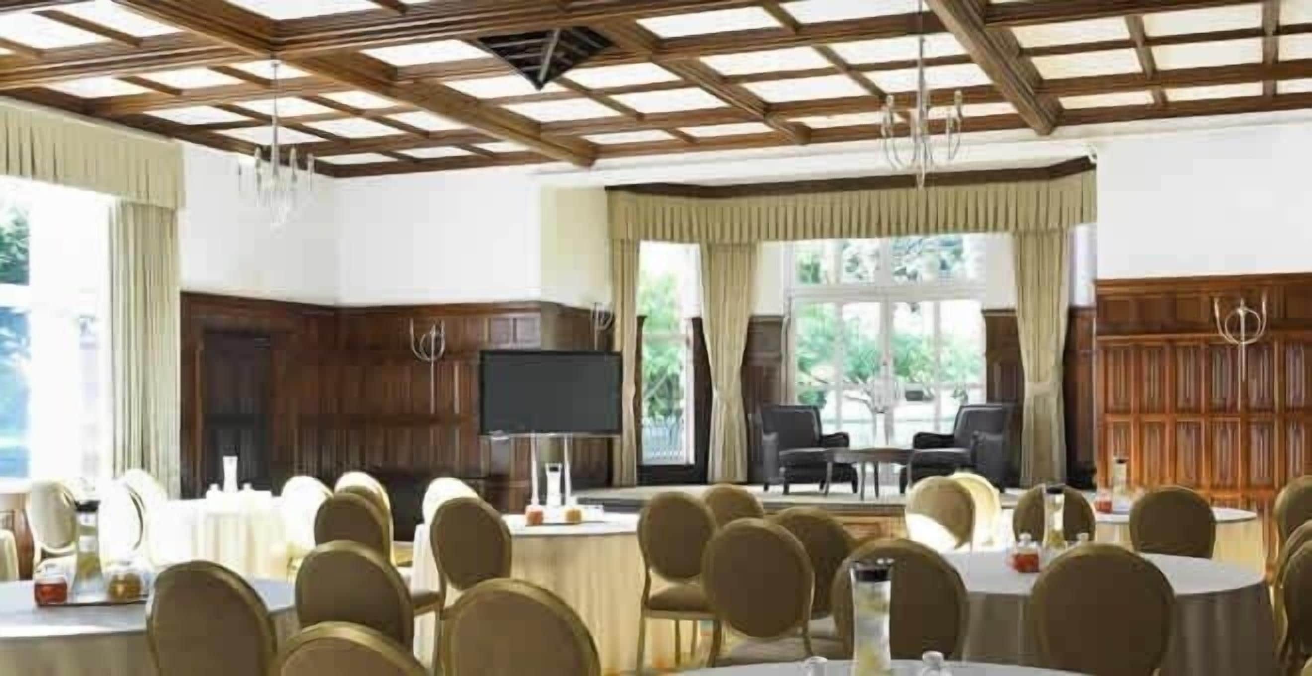 Un salón de conferencias con mesas y sillas redondas, una pantalla grande y un techo de madera.