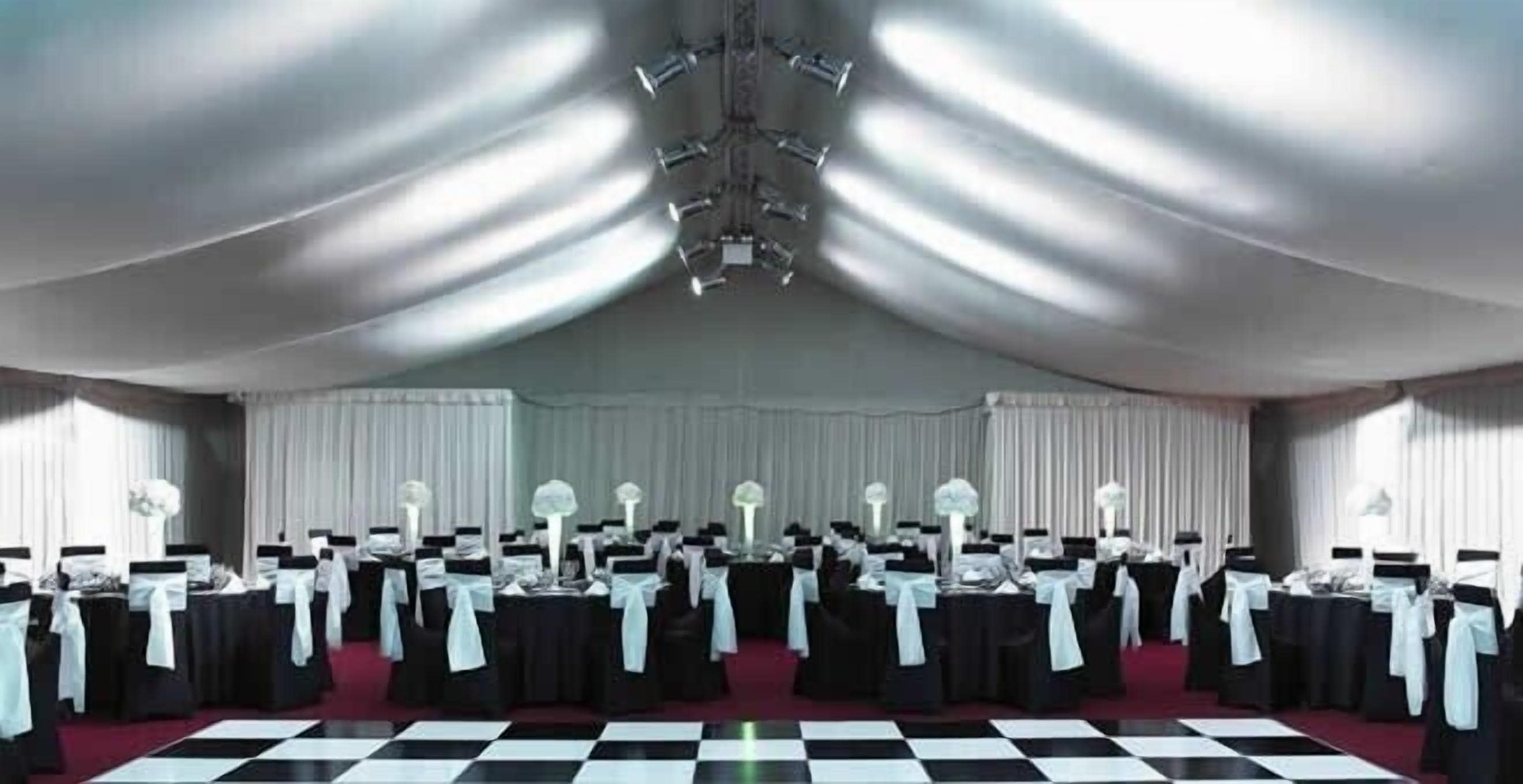A large hall with a checkered floor, rows of tables with white tablecloths, and black chairs with white sashes.