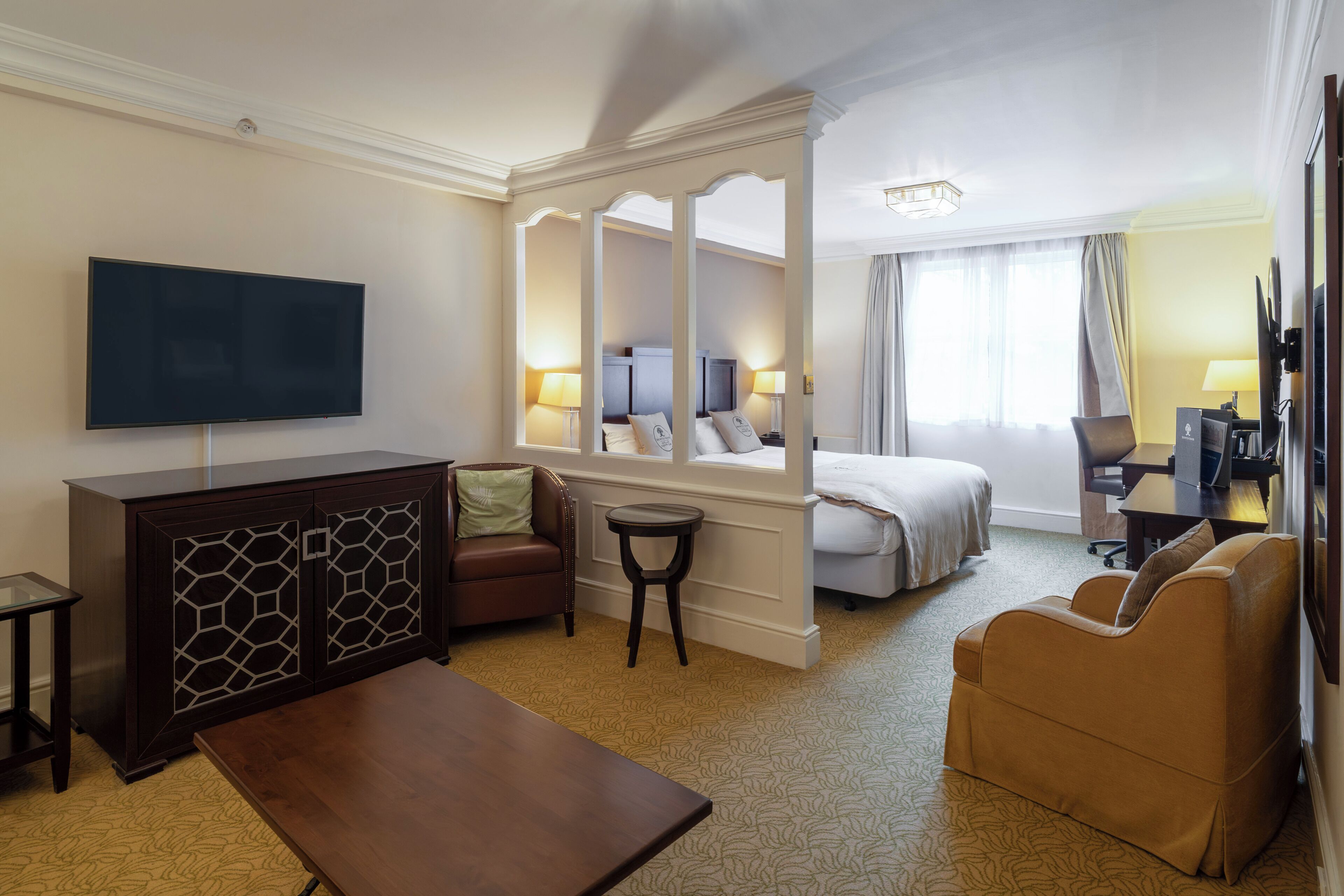 A hotel room with a bed, a sofa, a TV, a desk, and a mirror.