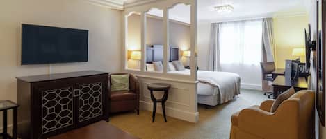 Una habitación de hotel con una cama, un sofá, un televisor, un escritorio y un espejo.