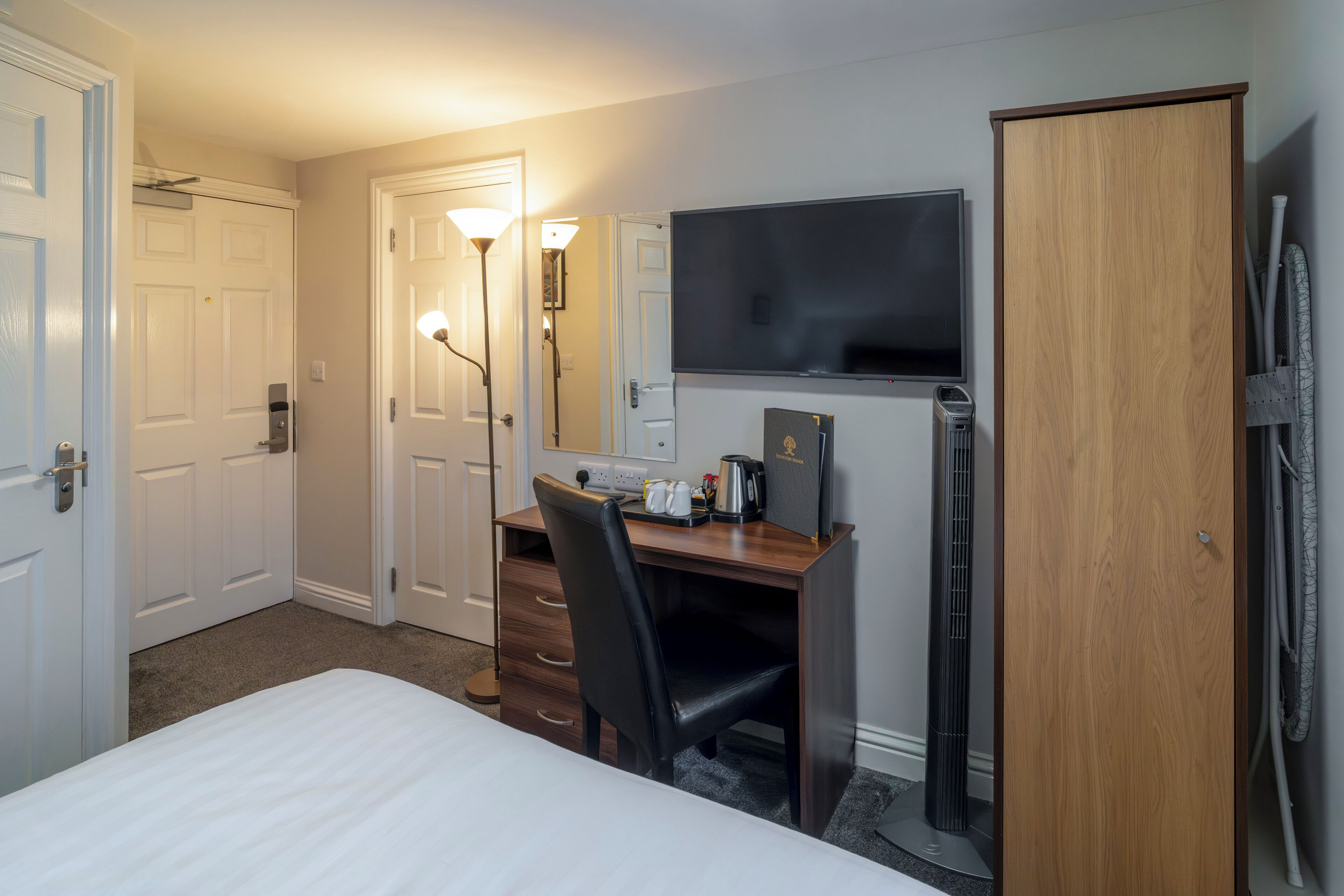 A hotel room with a bed, a desk with a chair, a TV, and a wardrobe.
